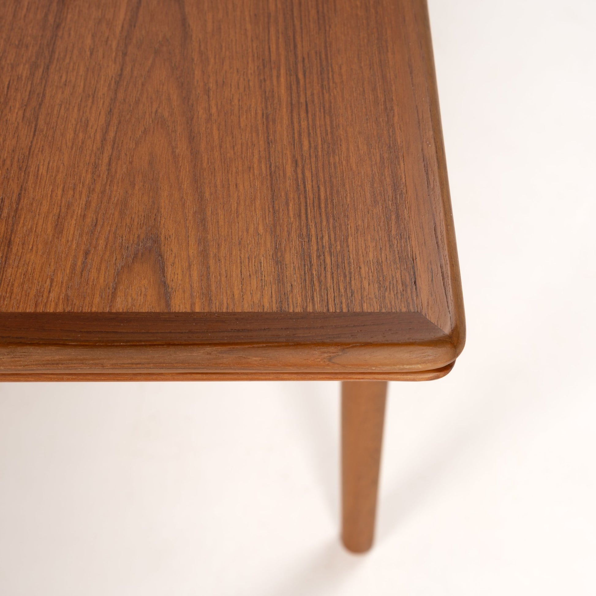 Corner close-up of wooden table top with fine grain texture and rounded edges on slender round leg in warm brown tone