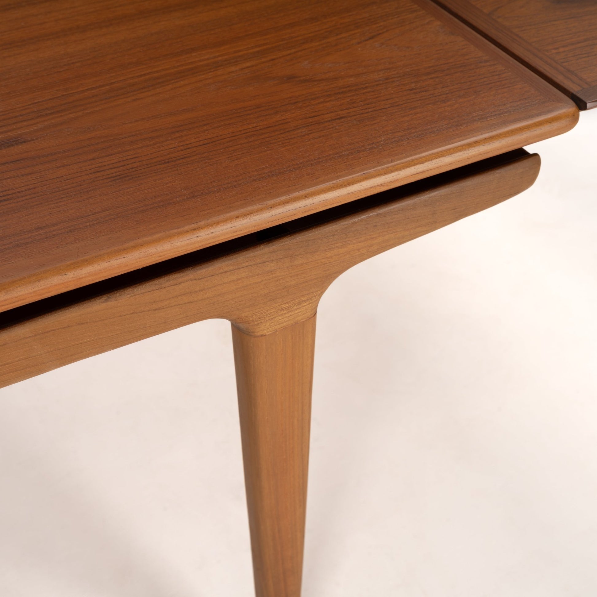 Close-up of smooth wooden dining table with rounded edges and tapered leg in warm medium brown finish