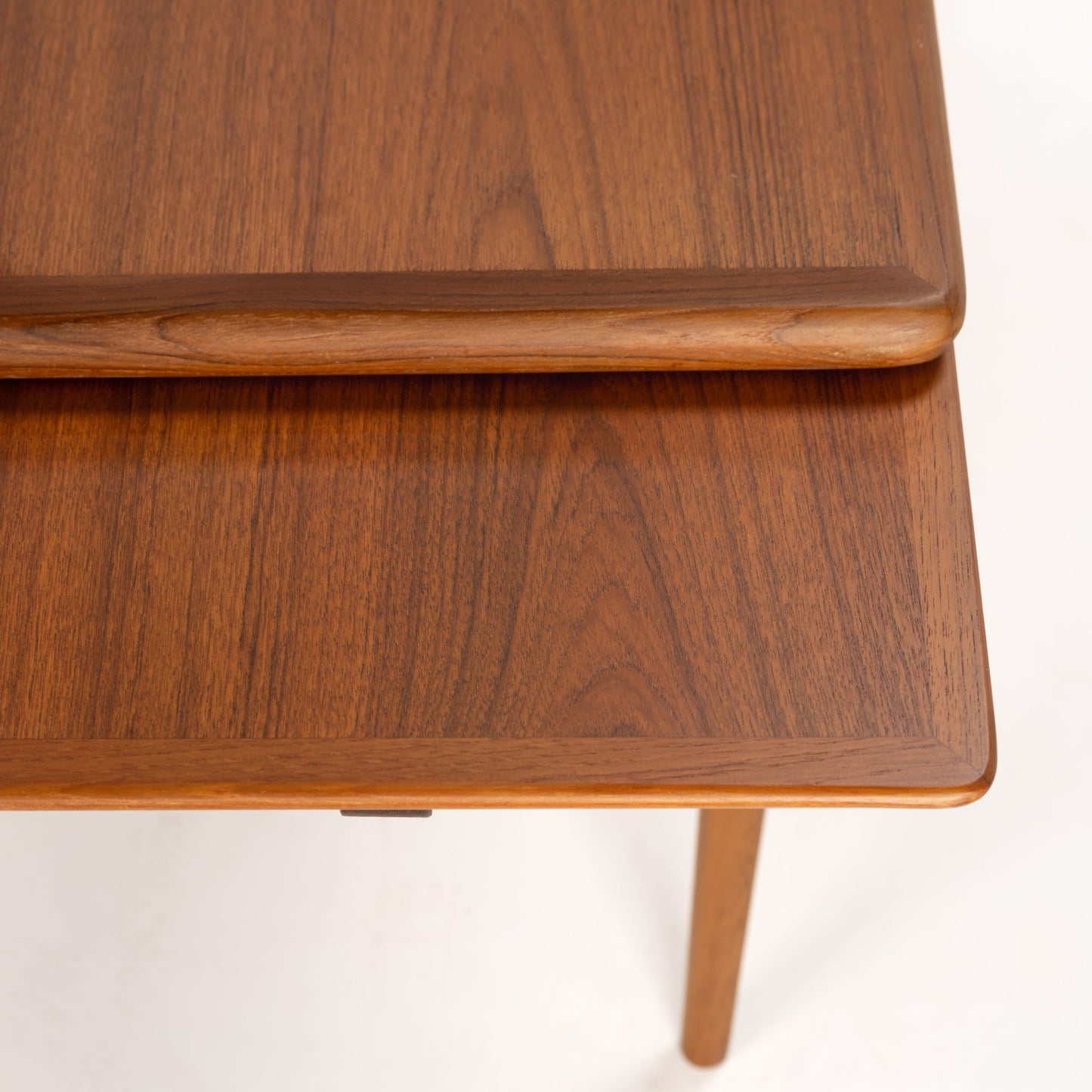 Close-up of smooth carved edge extendable wooden table top with rich walnut grain and tapered leg below