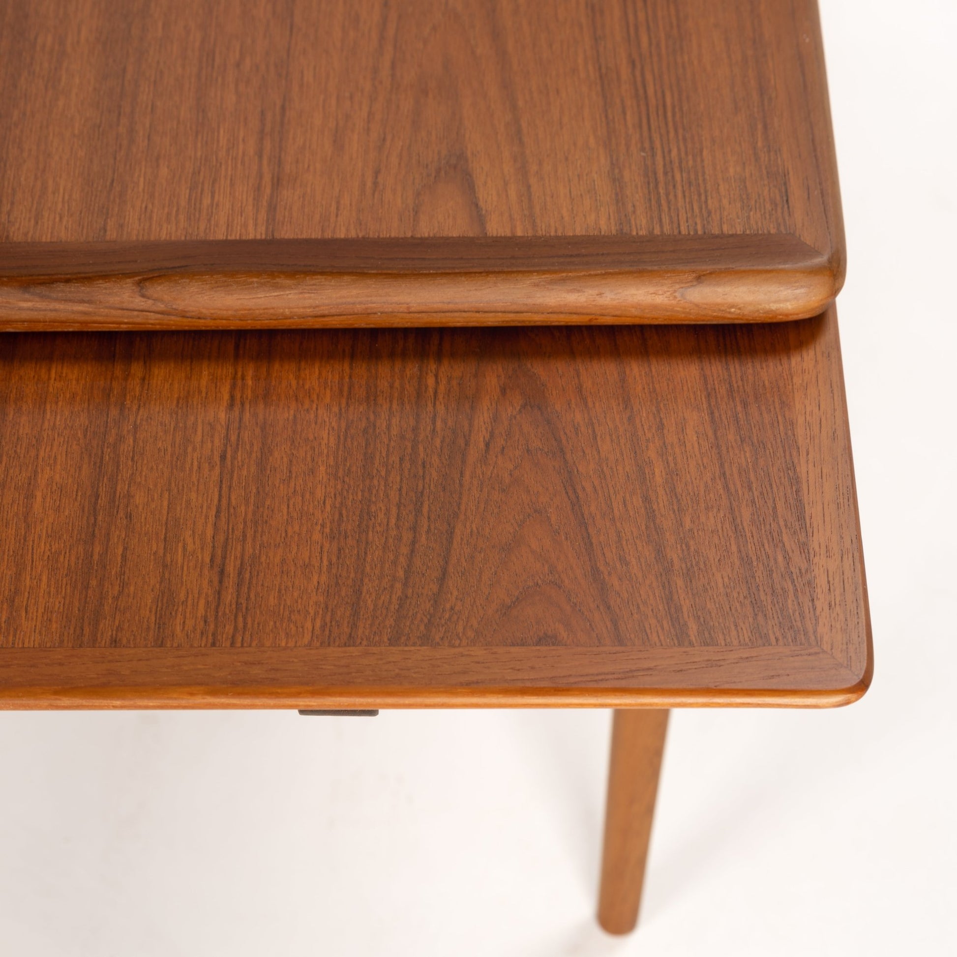 Close-up of smooth carved edge extendable wooden table top with rich walnut grain and tapered leg below