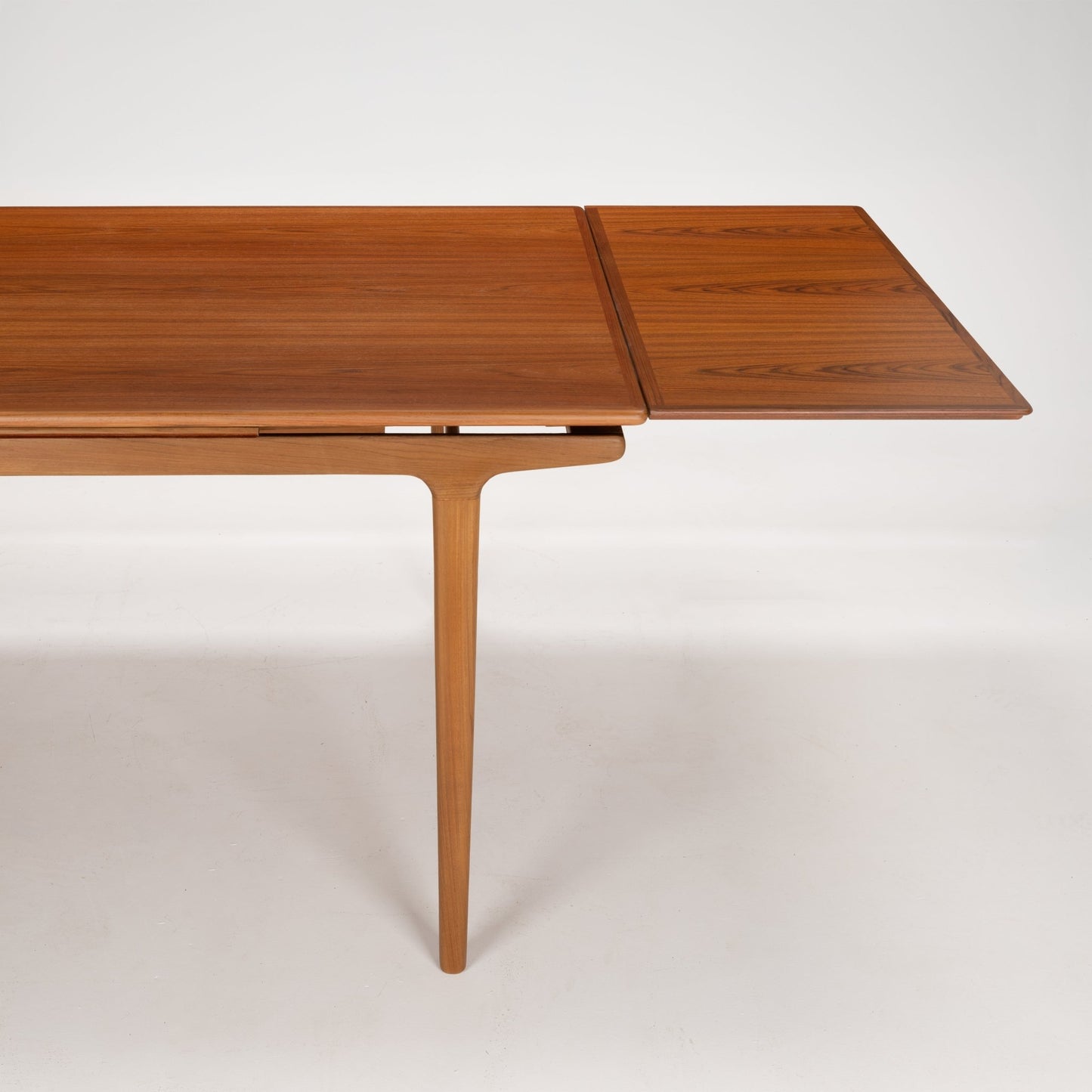 Mid-century wooden extending dining table with slender tapered legs and warm teak grain finish on white background