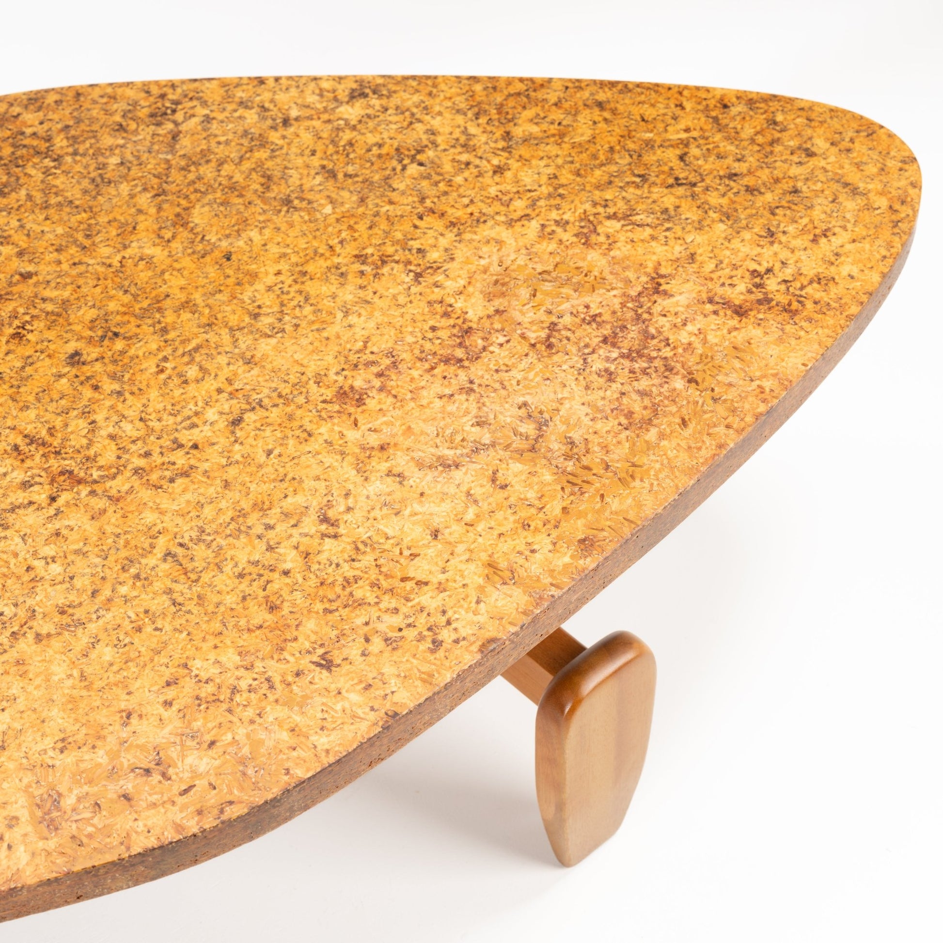 John Keal 'Outrigger' Coffee Table close-up showing the warm, textured cork surface with organic triangular shape and a sculptural wooden leg, embodying mid century modern furniture design.