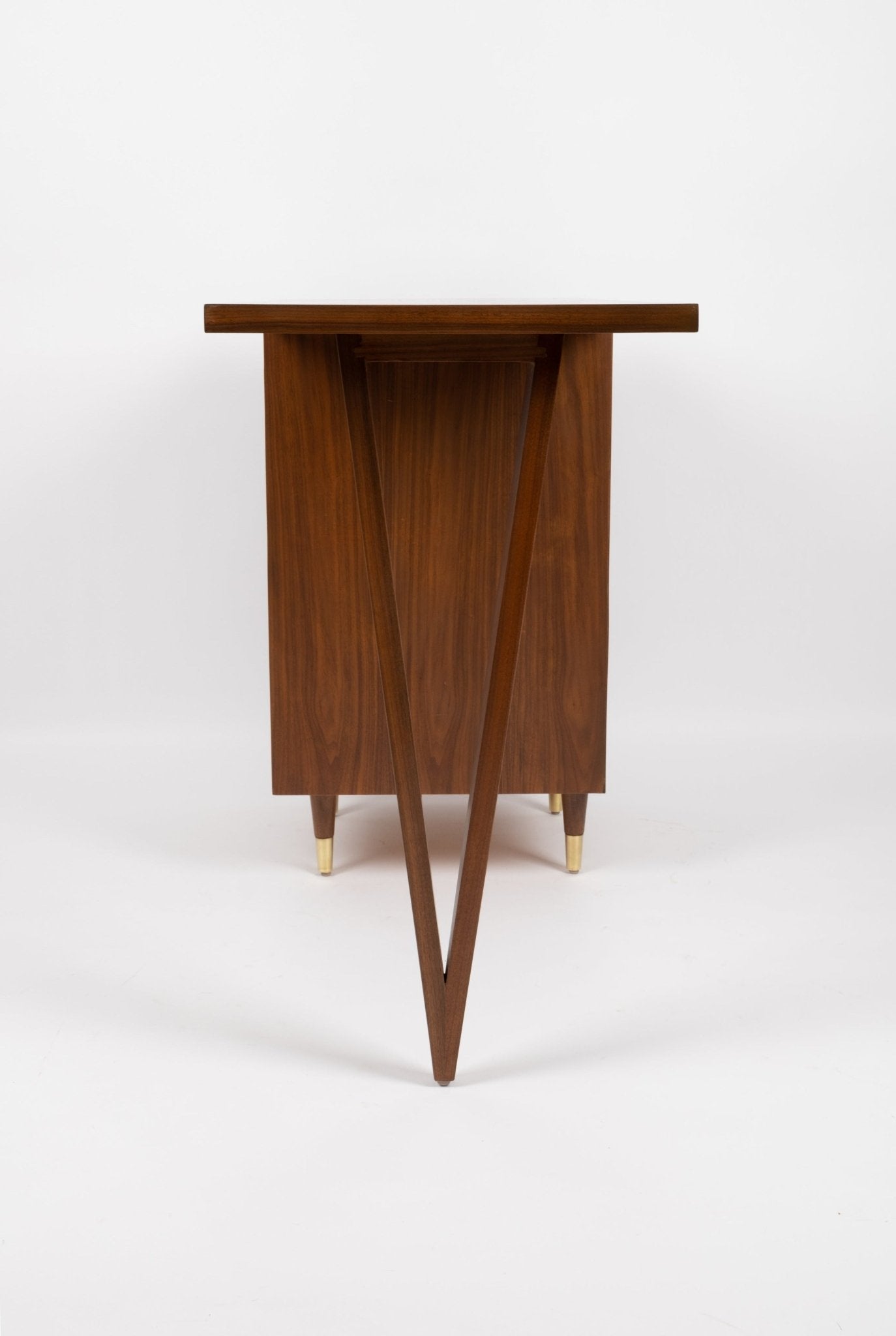 Mid-century modern John Stuart desk with triangular leg design, three drawers, brass handles, and brass-capped tapered legs.