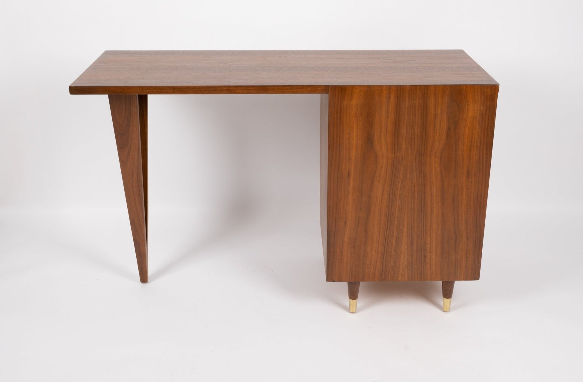 Mid-century modern John Stuart wooden desk with triangular legs, three drawers with brass handles, and brass feet.