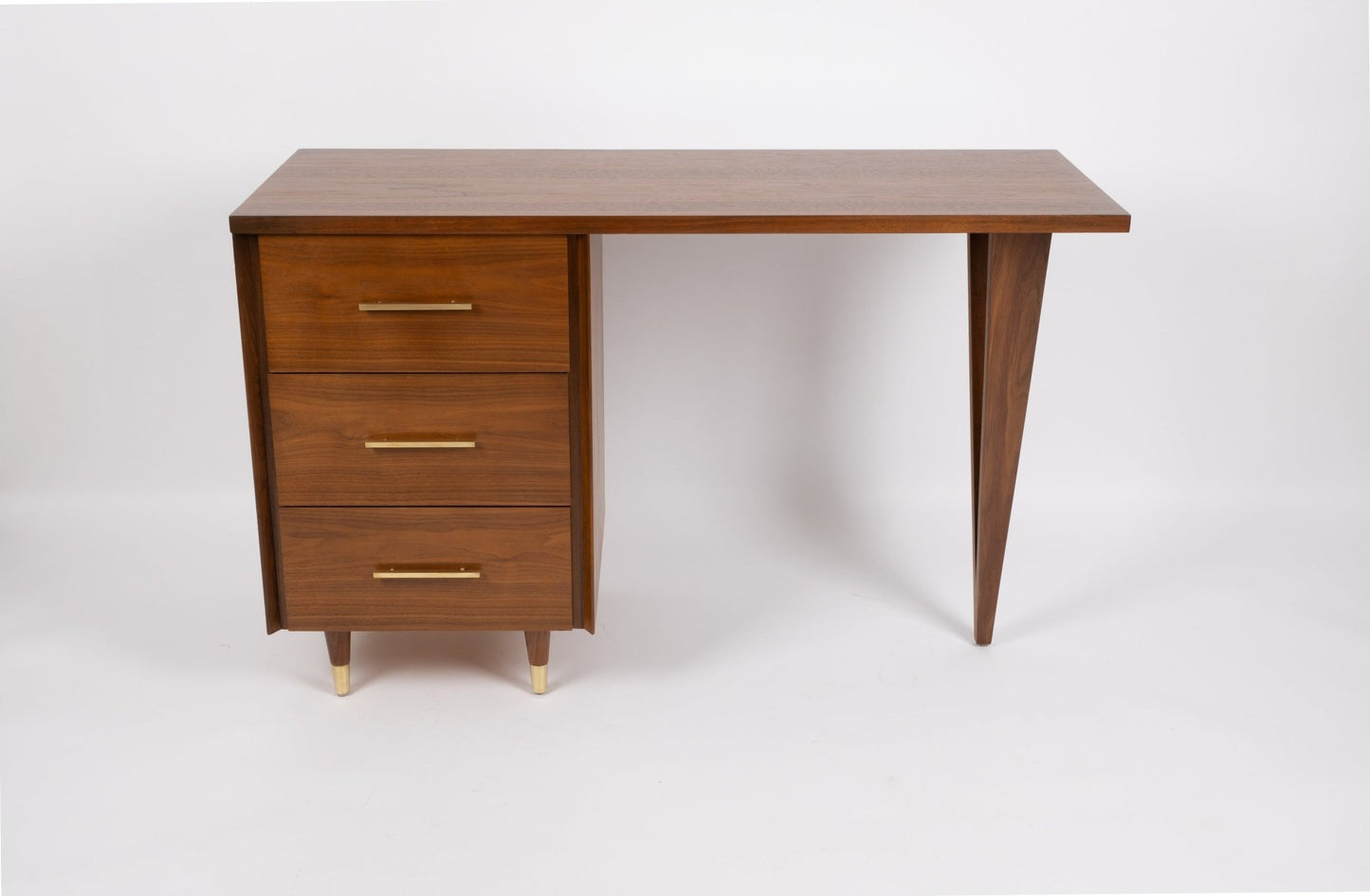 Mid-century modern John Stuart desk with triangular tapered legs, three drawers with brass handles and feet in wood finish
