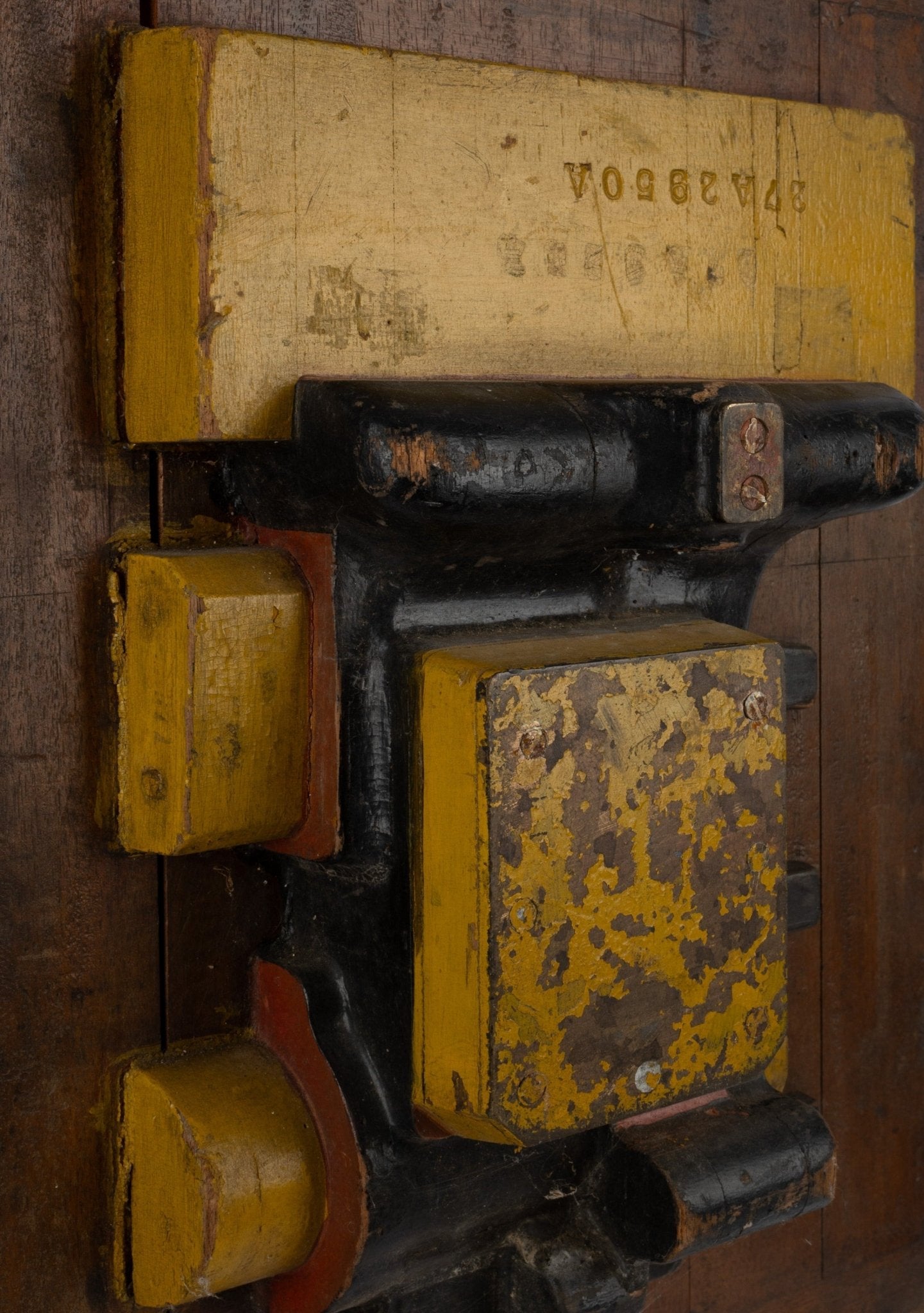 Two-sided industrial wooden machine mold sculpture with metal handle and worn yellow and black patina on wood background