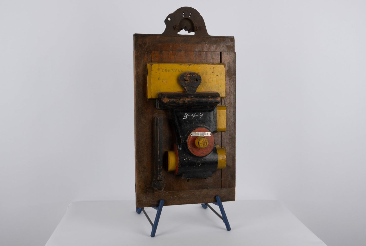 Two-sided vintage wooden industrial machine mold with metal handle and vibrant patina on display stand