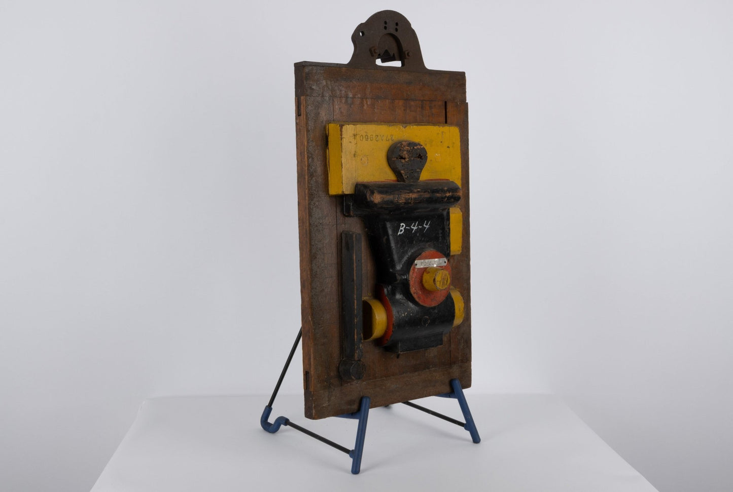 Two-sided wooden industrial machine mold sculpture with metal handle and vibrant patina on a minimalist stand.