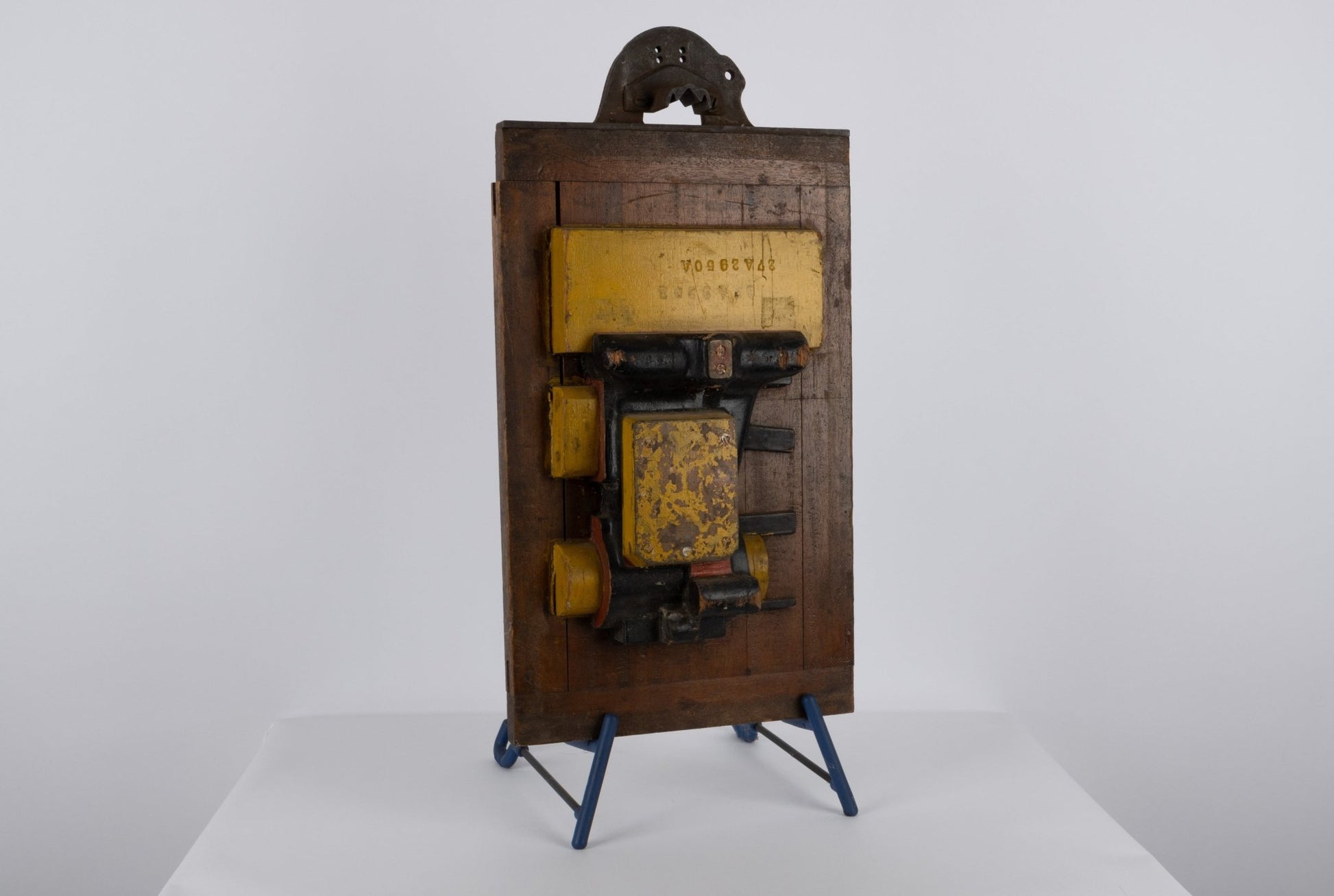 Two-sided wooden industrial machine mold with metal handle and vibrant patina displayed on blue stand.