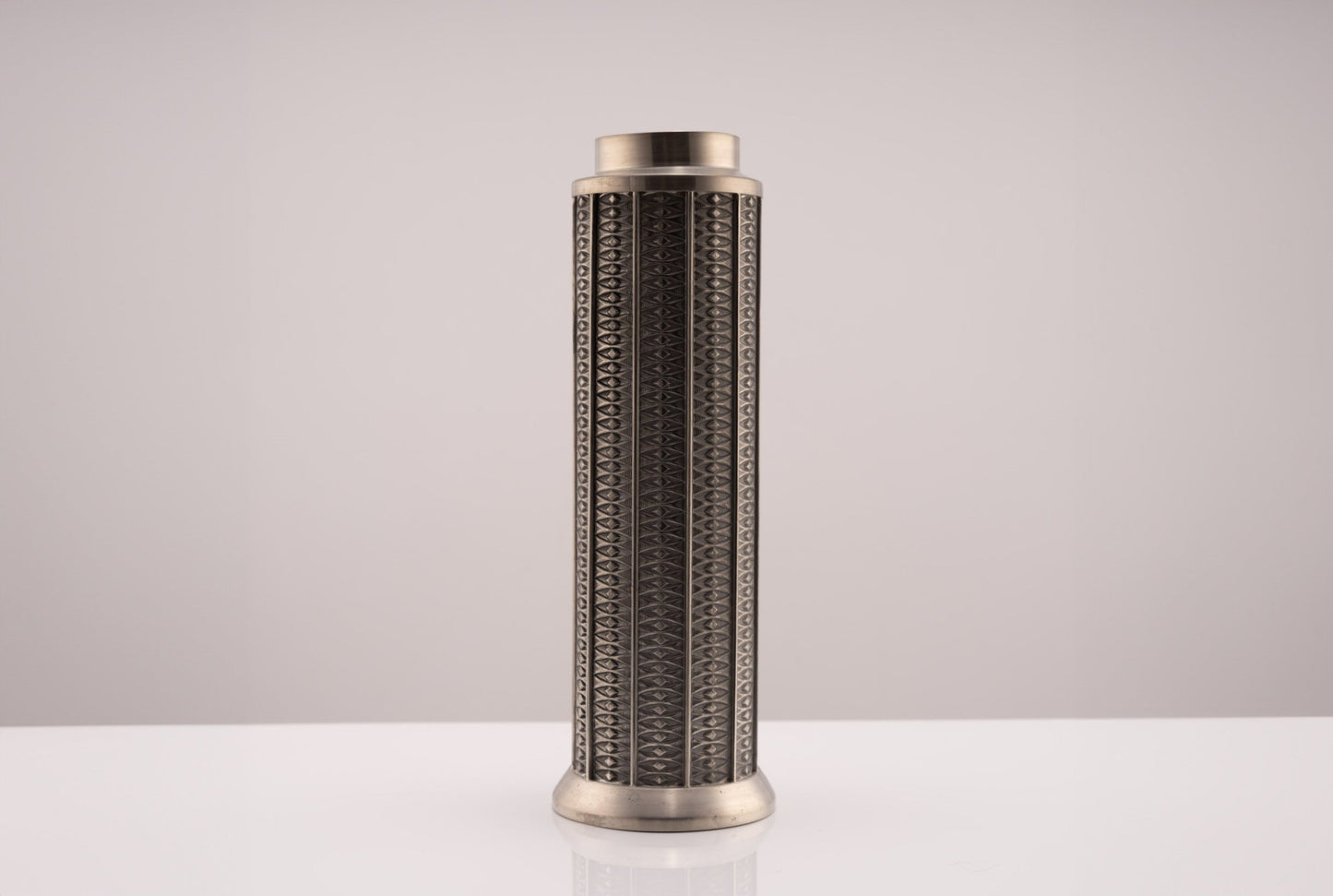 Tall cylindrical Mastad pewter vase with engraved diamond-shaped column pattern and marked bottom on white surface