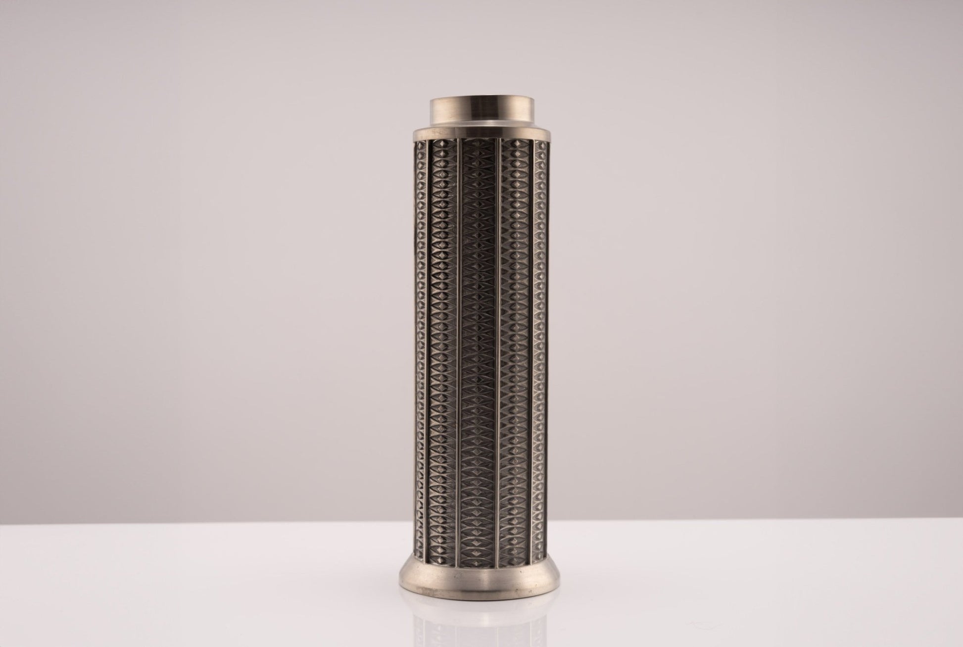 Tall cylindrical Mastad pewter vase with engraved diamond-shaped column pattern and marked bottom on white surface