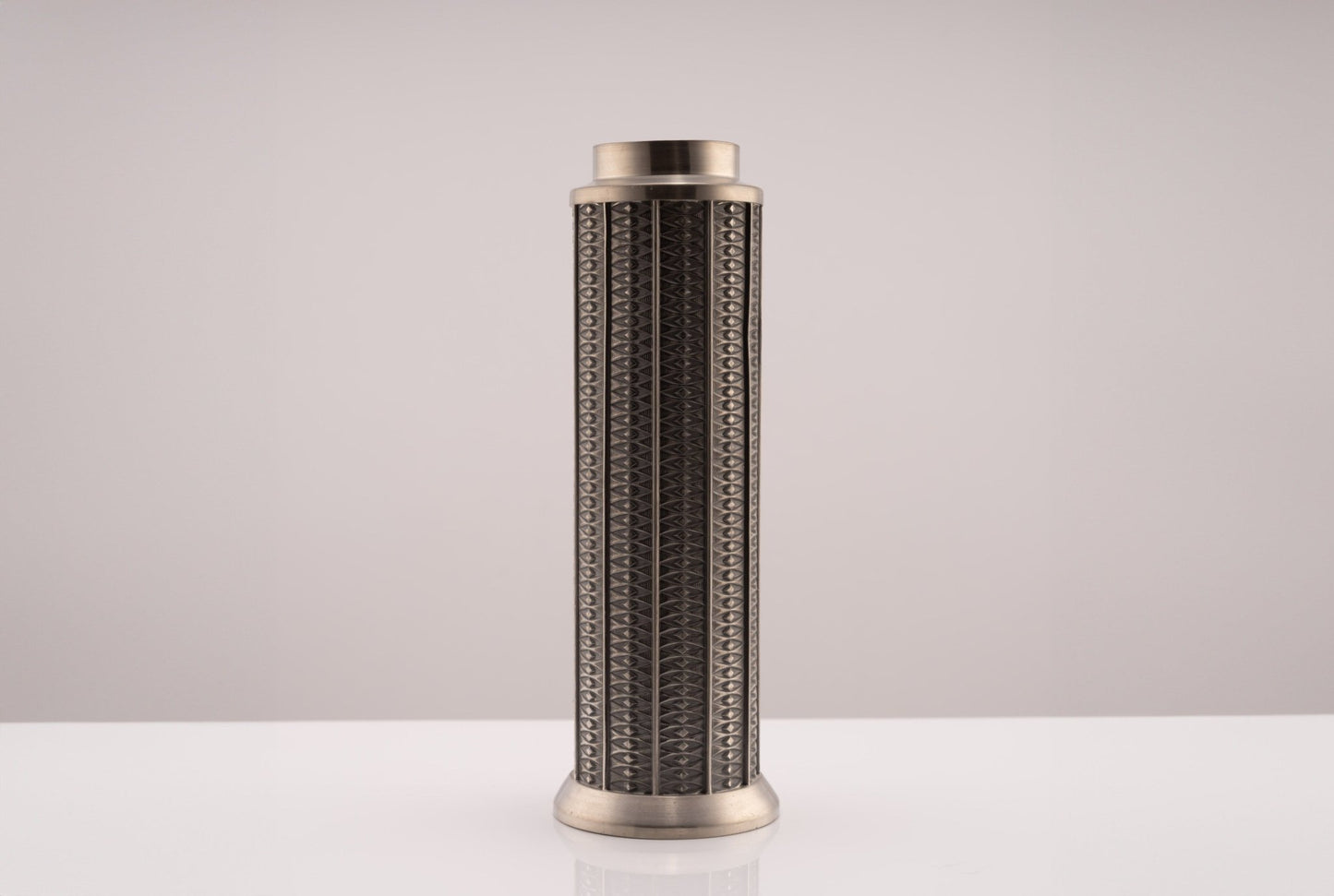 Cylindrical Mastad pewter vase with engraved diamond-shaped columns and marked base, set against a neutral background.