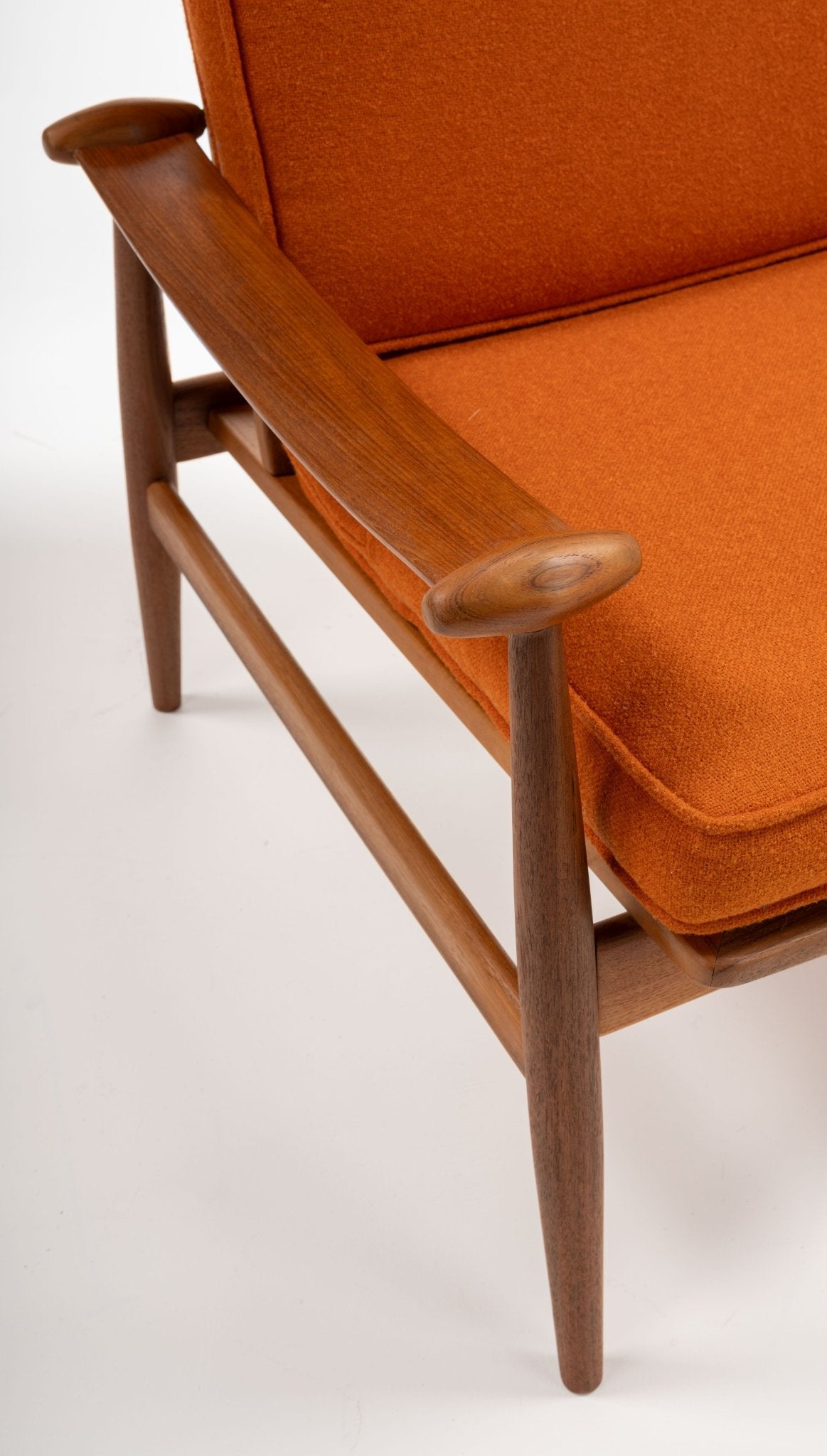 Close-up of mid-century modern teak armrest and orange fabric cushion on Finn Juhl Spade Armchair from 1950s Denmark.