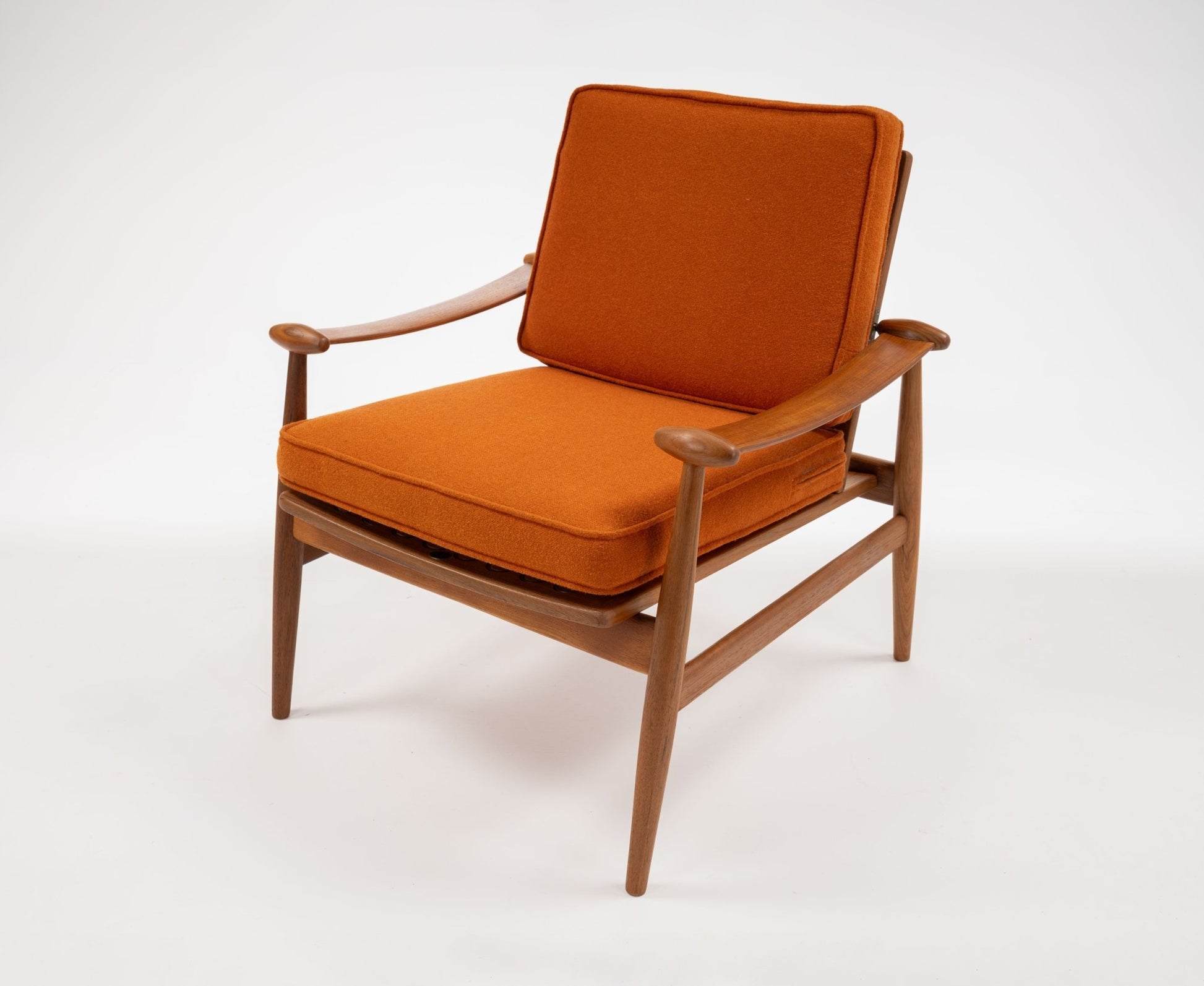 Mid-century modern teak armchair with sculpted spade-shaped arms and burnt orange cushions on white background