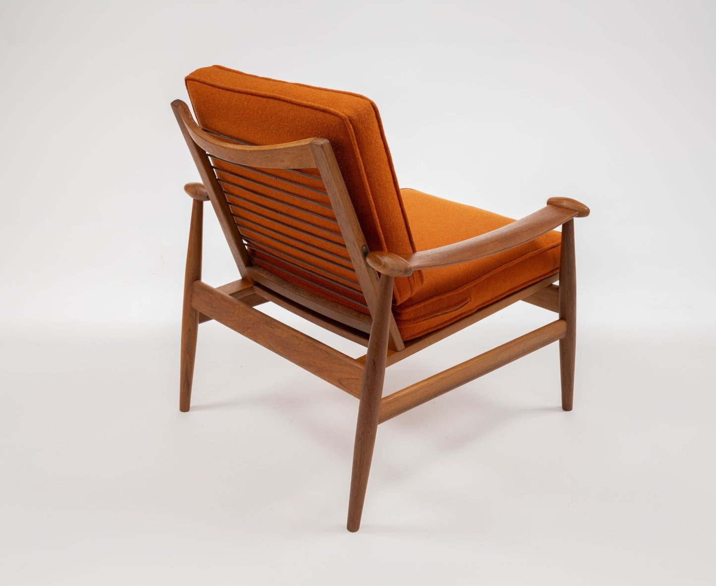 Mid-century modern Model 133 Spade Armchair by Finn Juhl with solid teak frame and burnt orange cushions on white background.