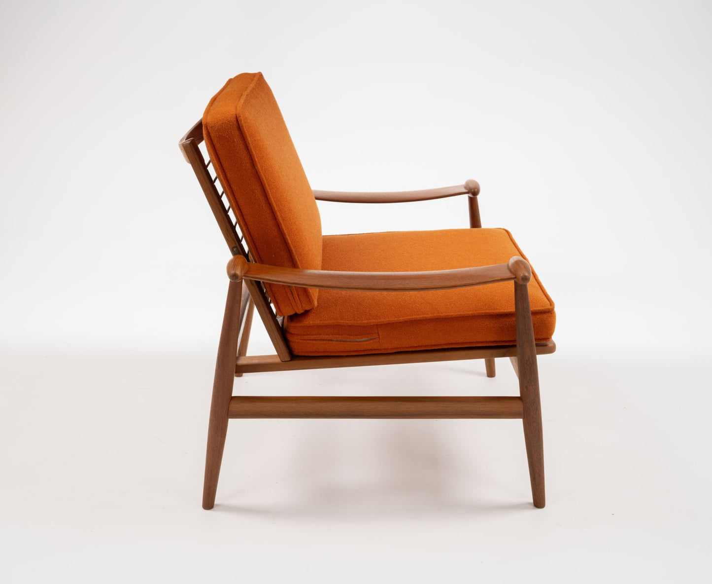 Mid-century modern teak armchair with spade-shaped arms and burnt orange cushions on white background