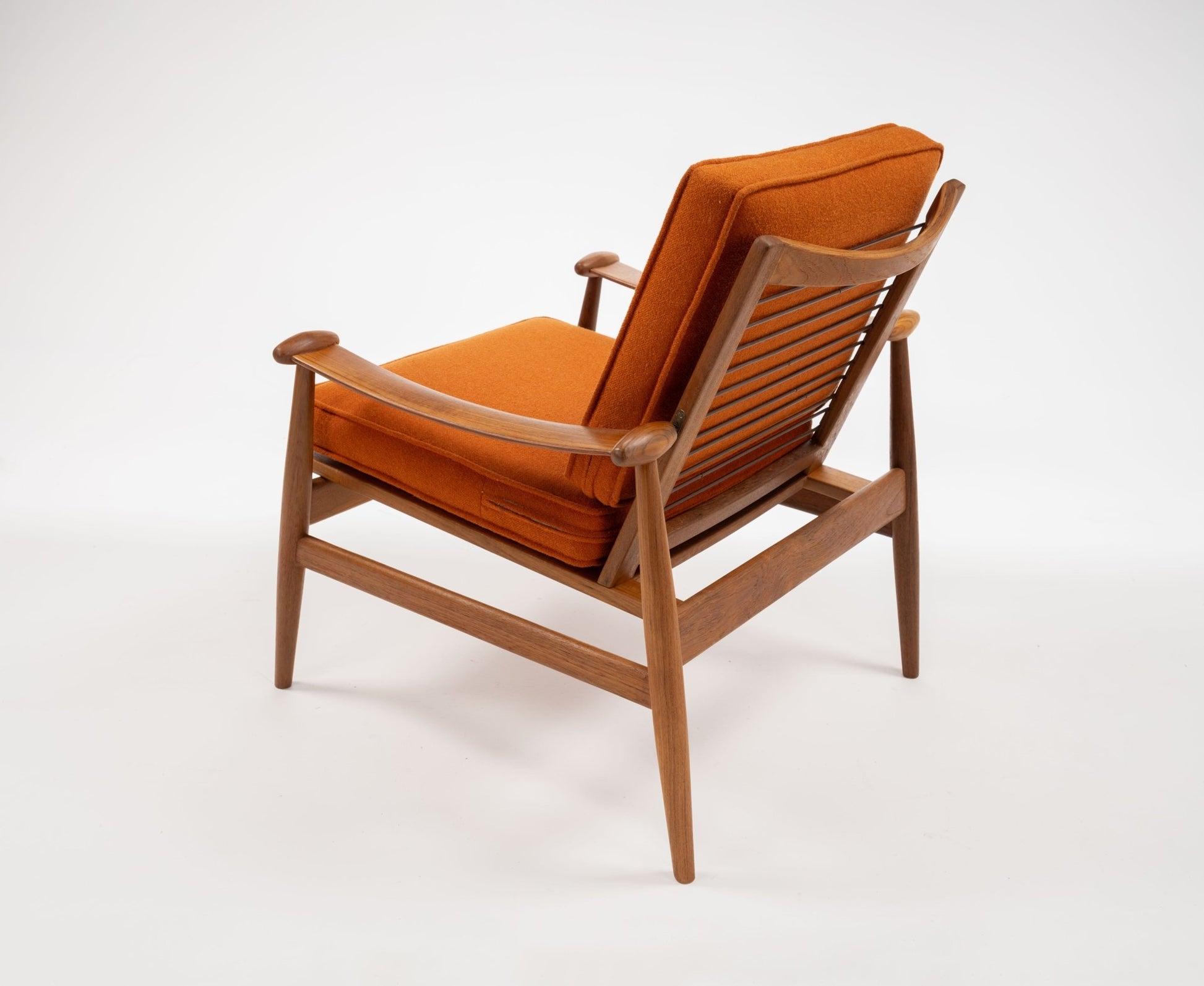 Mid-century modern teak spade armchair with orange upholstered cushions and sculpted wooden frame back view.