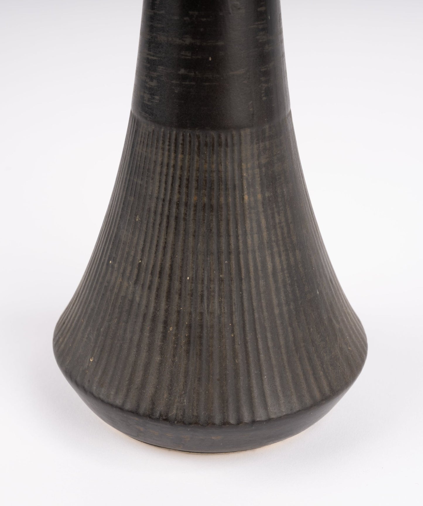 Close-up of Nelson McCoy pottery vase base with deep charcoal-black glaze and vertical ribbed texture