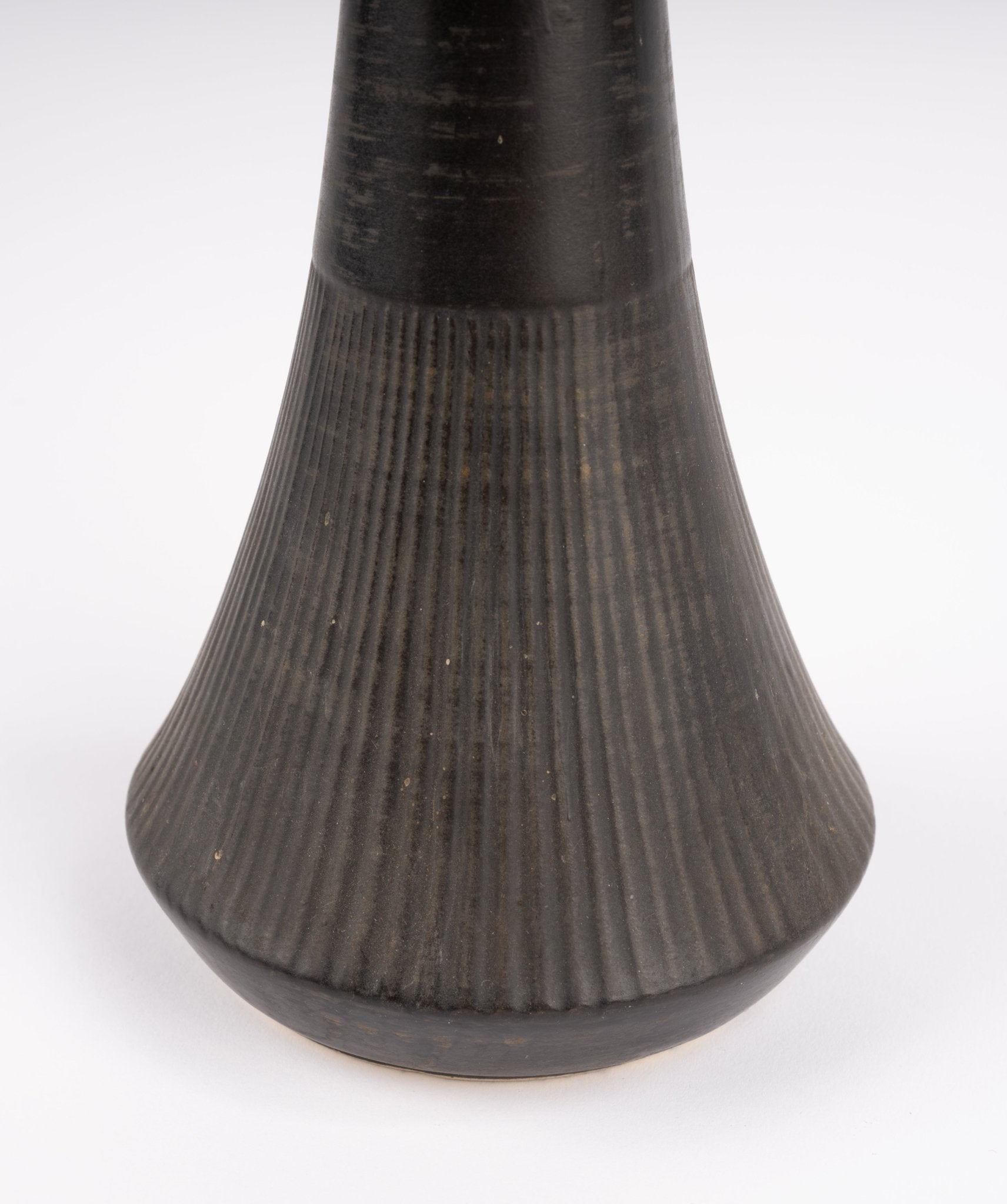 Close-up of Nelson McCoy pottery vase base with deep charcoal-black glaze and vertical ribbed texture
