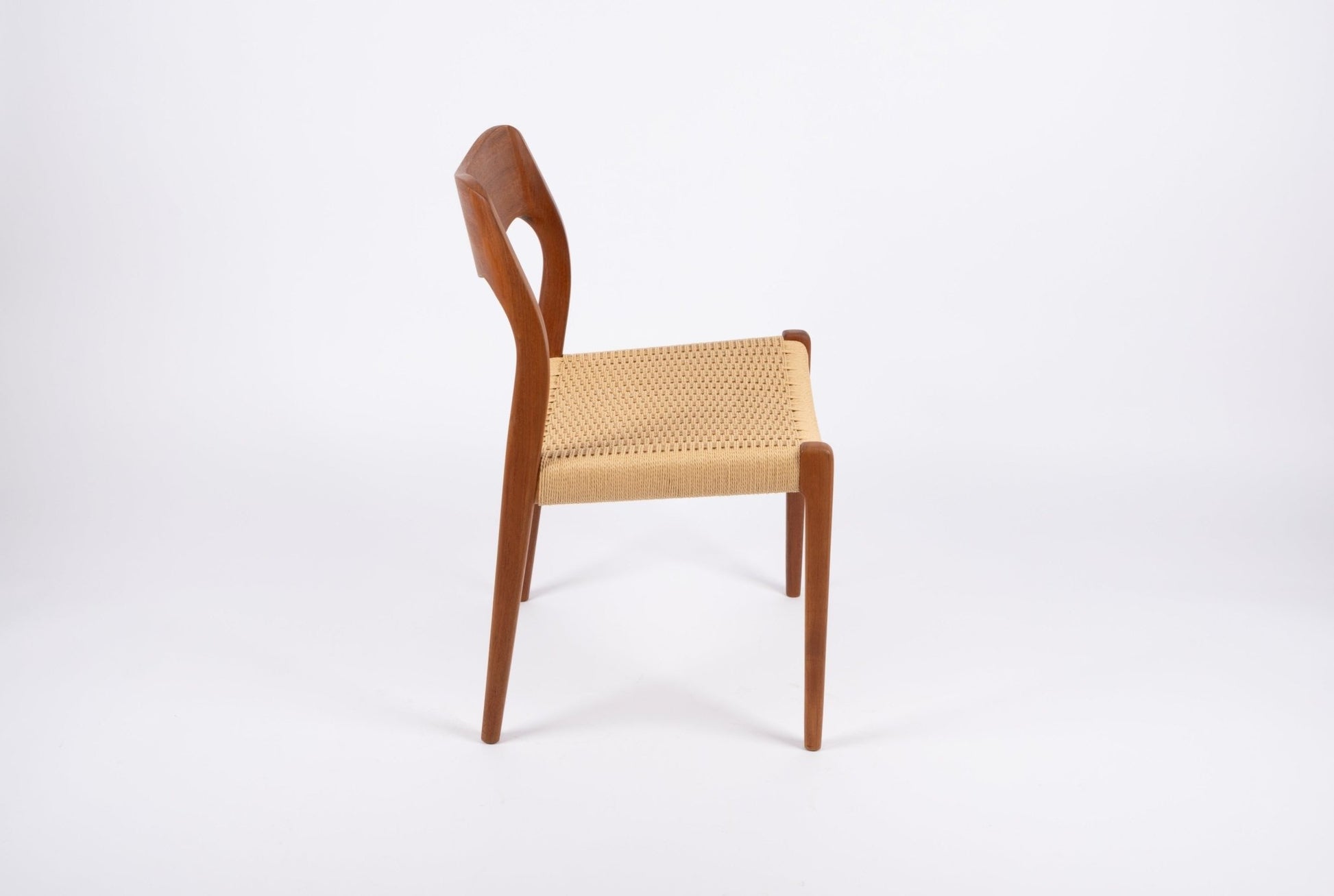 Mid-century modern Niels Moller dining chair in teak with sculpted backrest and woven Danish cord seat on white background