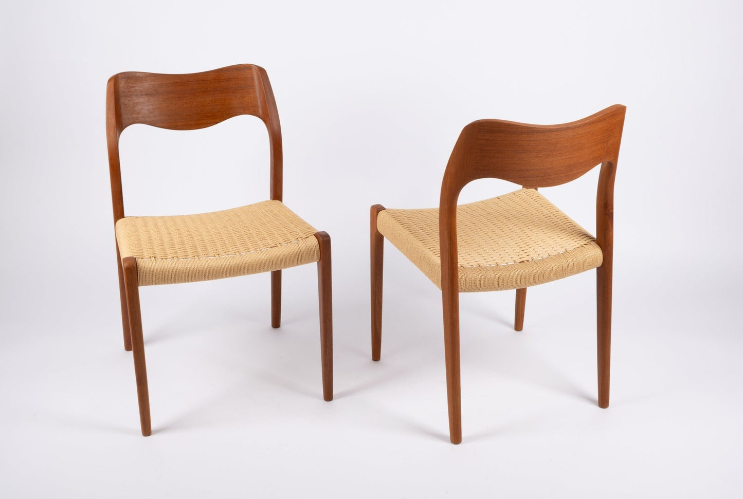 Pair of mid-century modern Niels Moller dining chairs with teak frames and woven Danish cord seats on white background