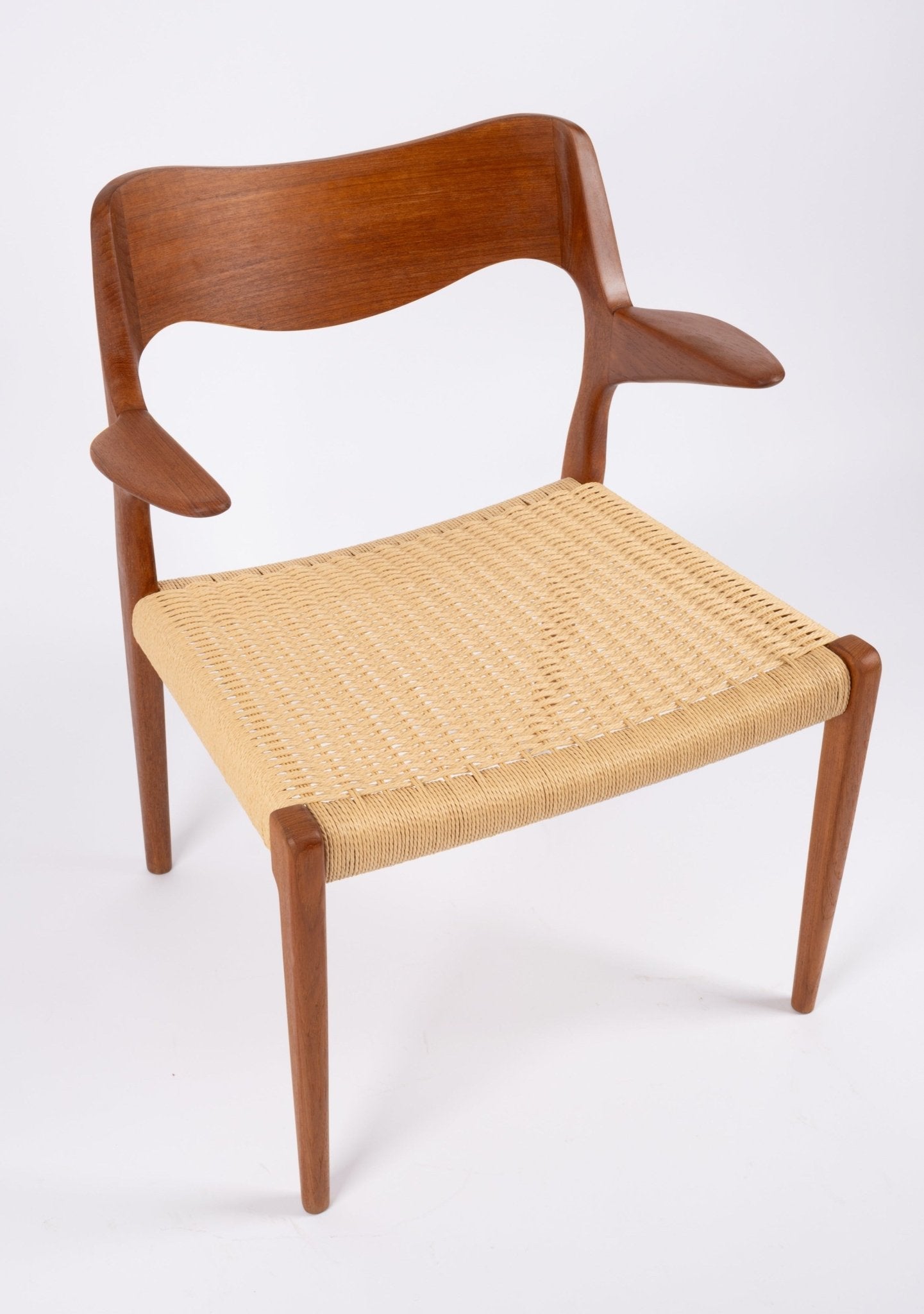 Mid-century modern solid teak dining chair with sculpted armrests and woven Danish cord seat on white background