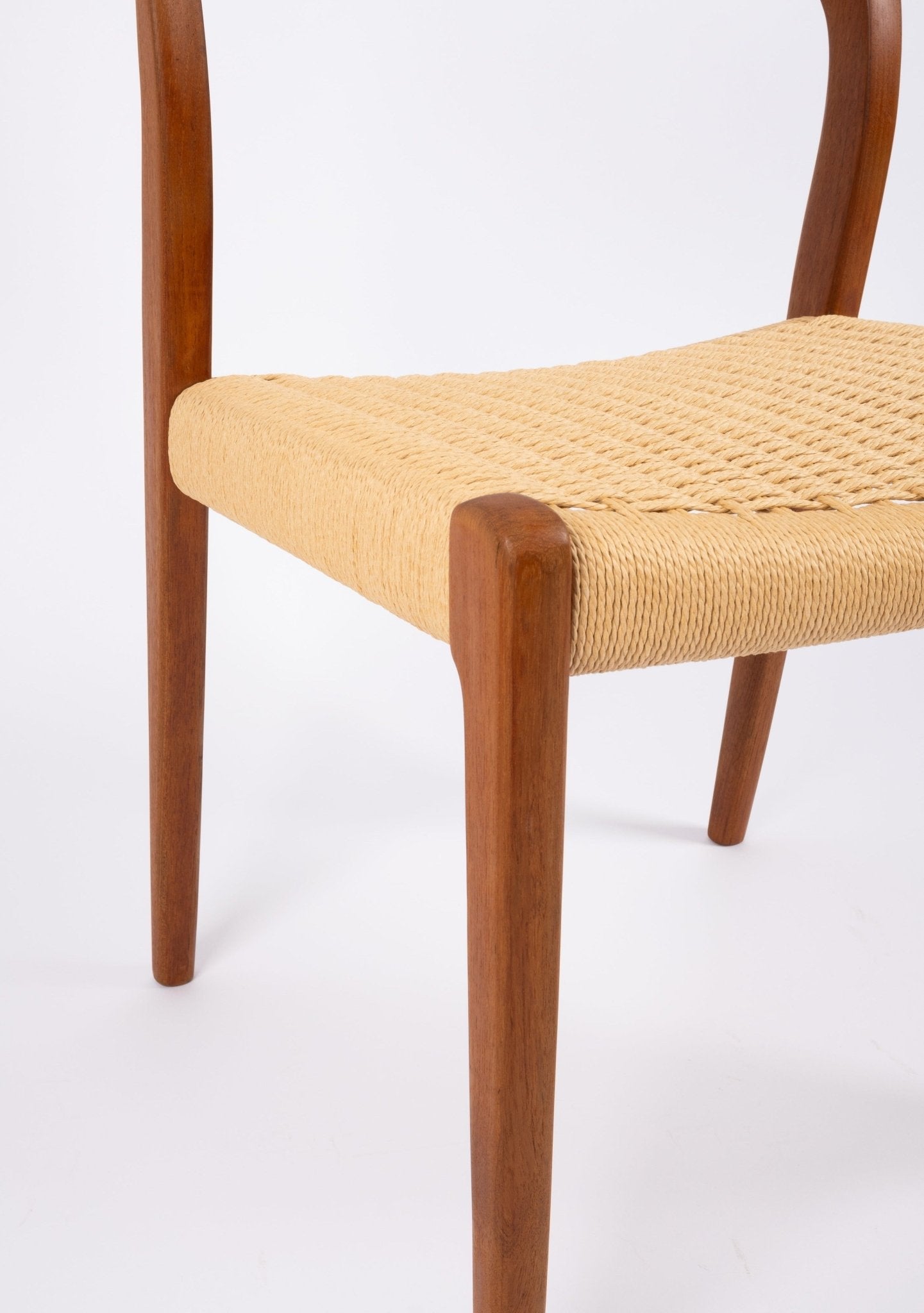 Close-up of mid-century modern teak dining chair with woven Danish cord seat and slender tapered legs on white background