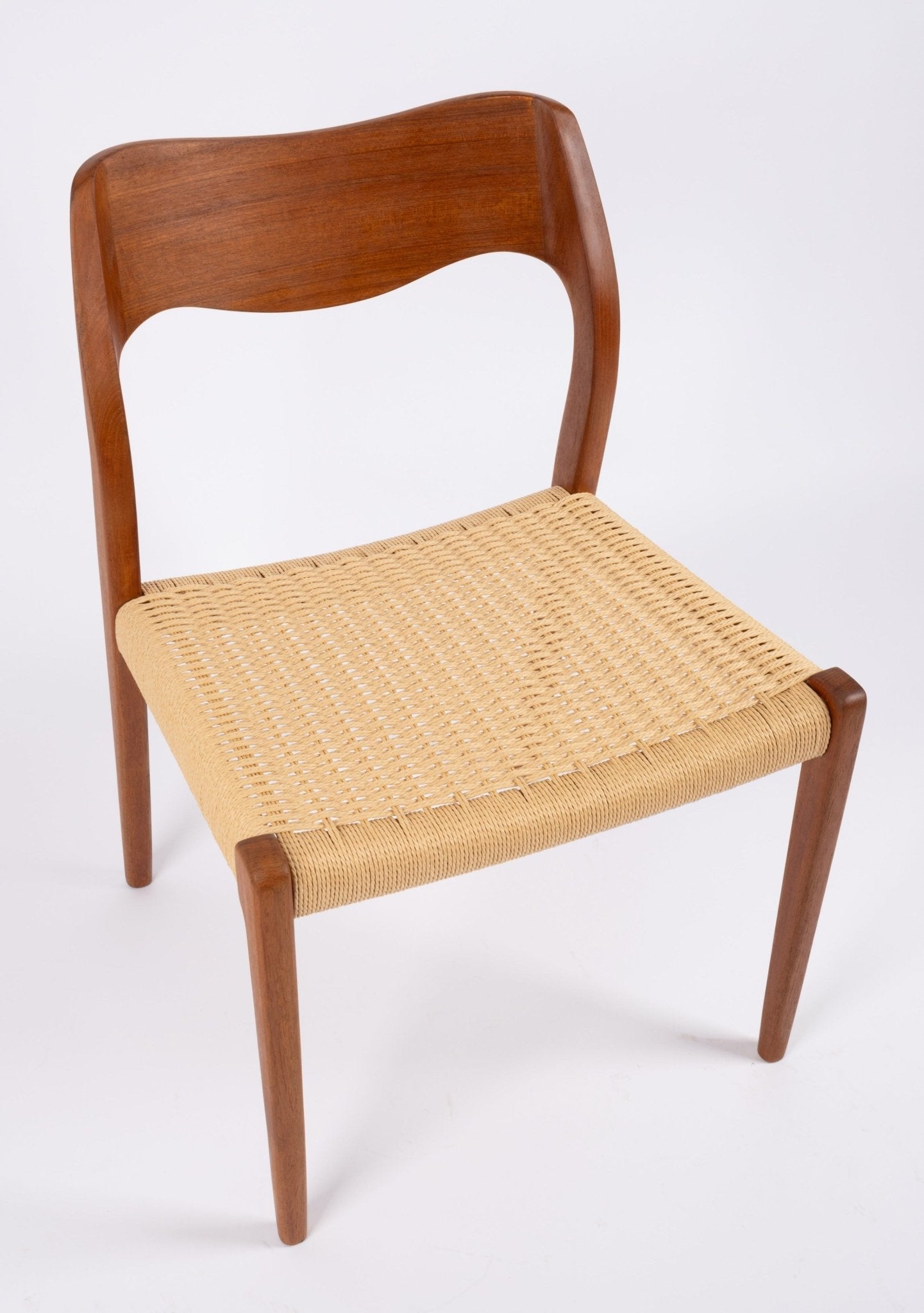 Mid-century modern Niels Moller dining chair with curved teak backrest and woven Danish cord seat on white background.