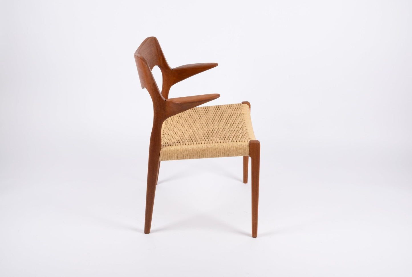 Side view of mid-century modern Niels Moller dining chair with sculpted teak frame and woven Danish cord seat