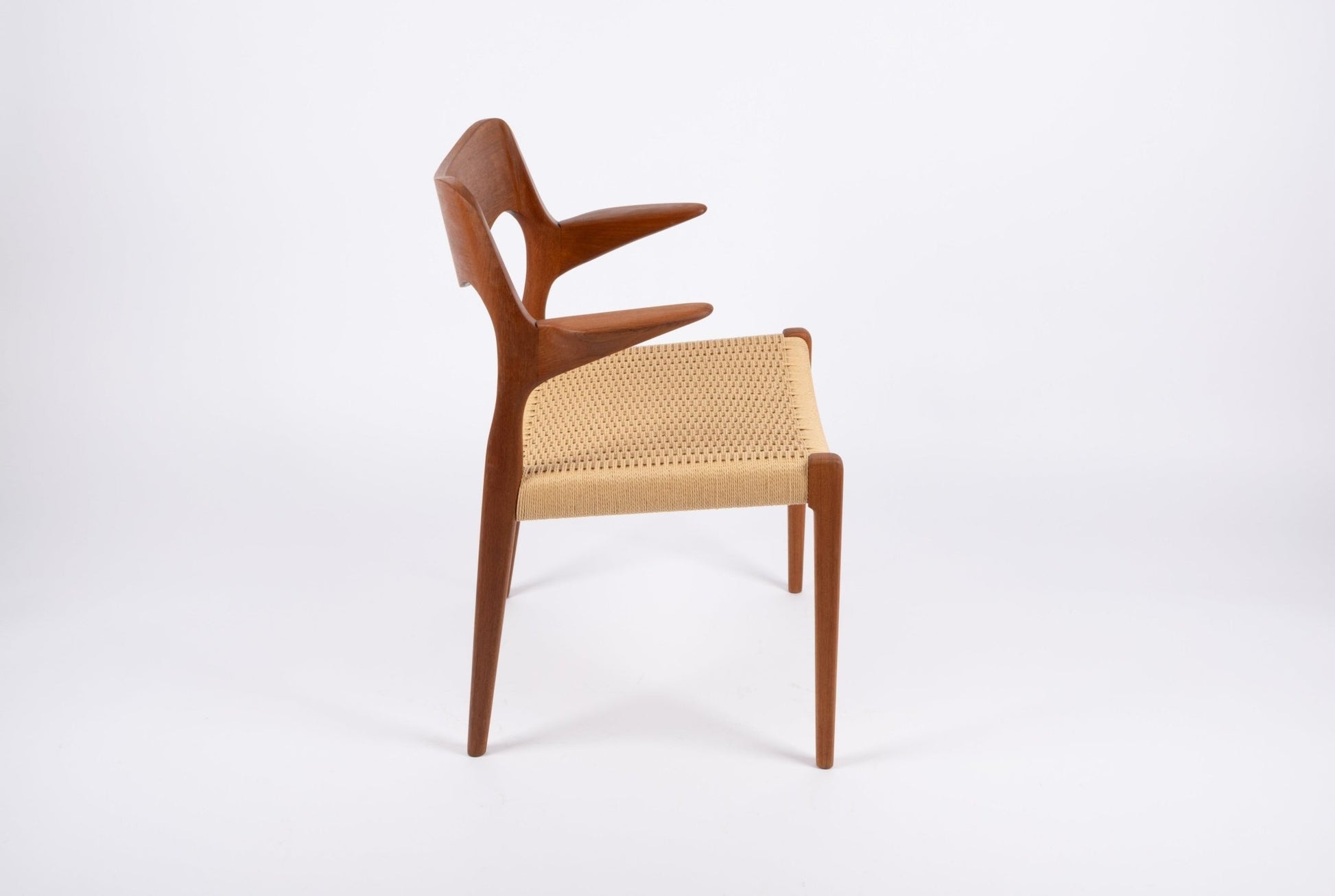 Side view of mid-century modern Niels Moller dining chair with sculpted teak frame and woven Danish cord seat