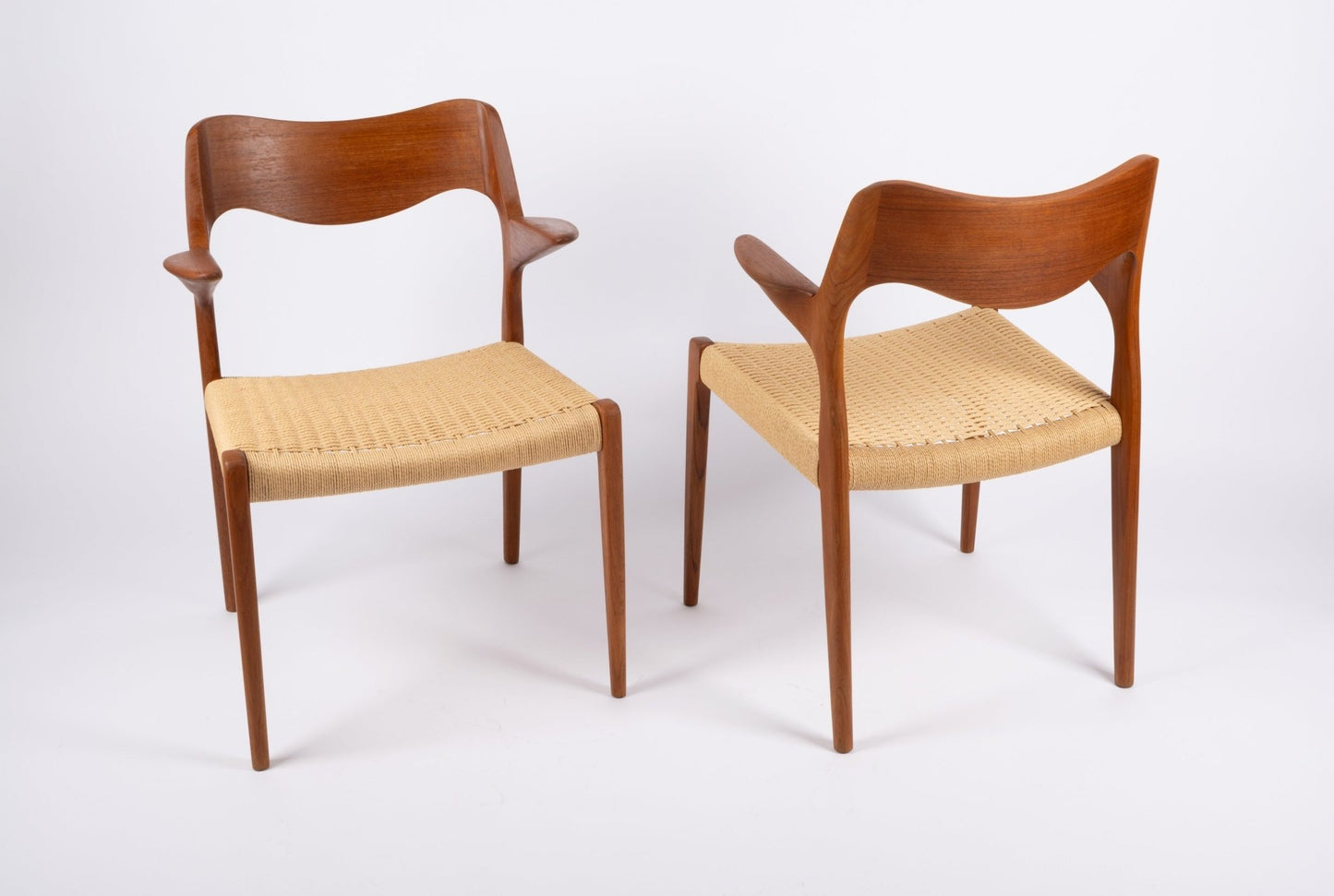 Pair of Niels Moller teak dining chairs with sculpted curved backs and woven Danish cord seats on white background