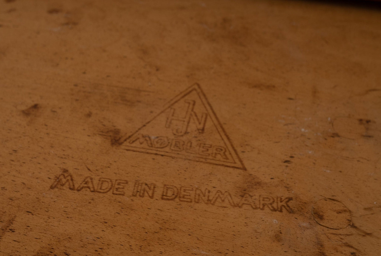 Close-up of HJN Mobler maker's mark and "Made in Denmark" stamp on vintage wooden furniture piece.