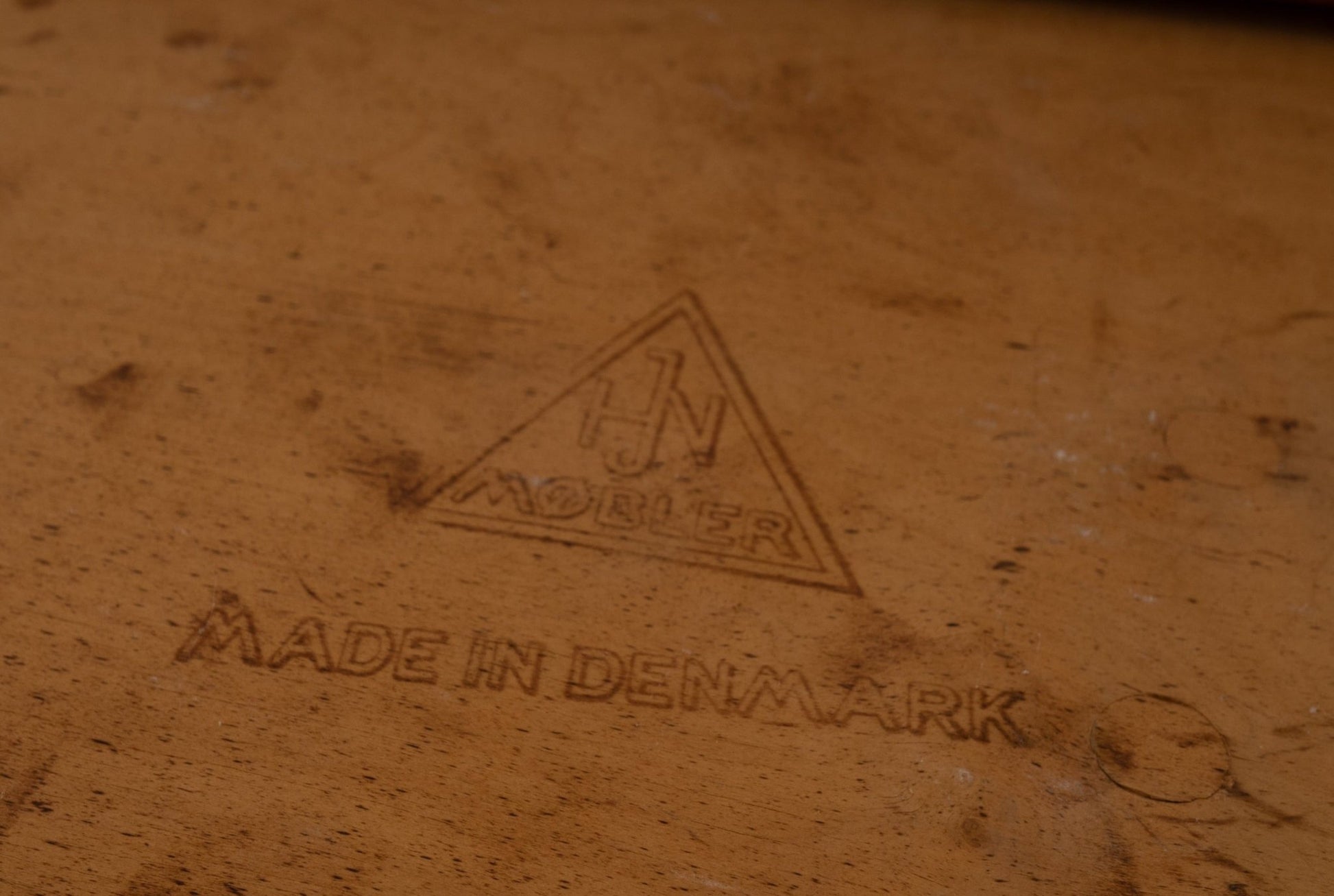 Close-up of HJN Mobler maker's mark and "Made in Denmark" stamp on vintage wooden furniture piece.