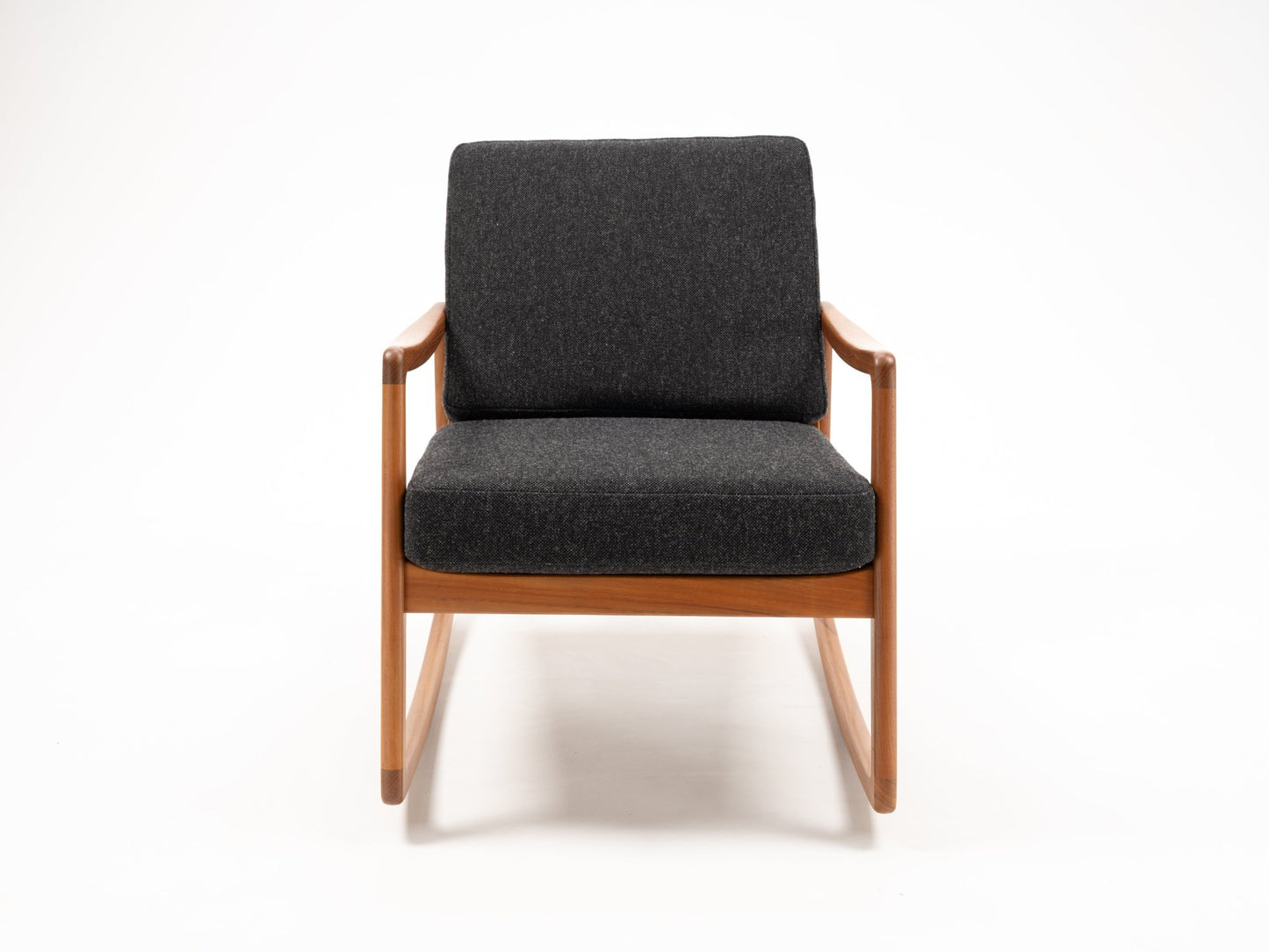Ole Wanscher teak rocking chair with sculpted armrests and dark upholstered seat and backrest on white background