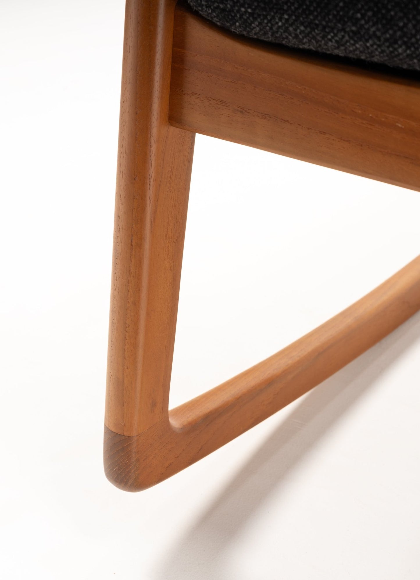 Close-up of mid-century modern teak rocking chair leg with smooth, curved design and warm wood finish on white background.