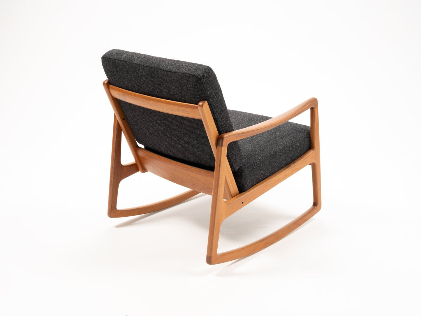 Ole Wanscher rocking chair with solid teak frame, sculpted armrests, and dark gray upholstered cushions on white background.