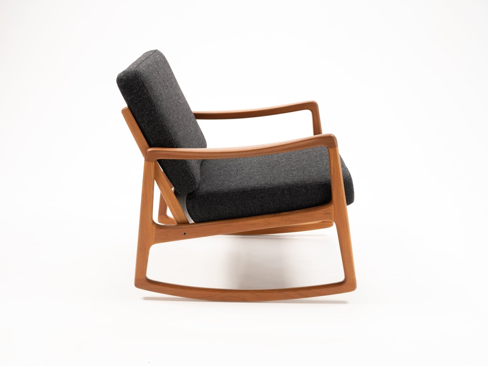Mid-century modern teak rocking chair with sculpted armrests and dark gray upholstered cushions on white background.