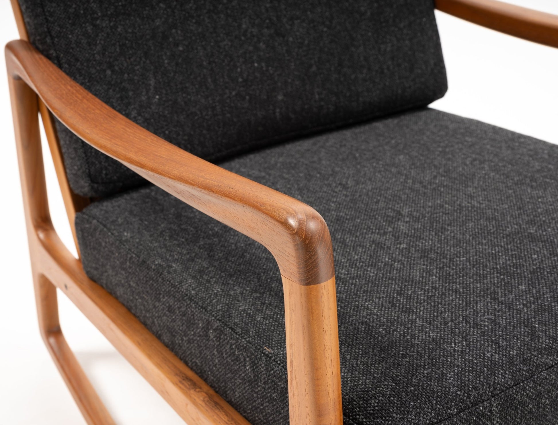 Close-up of Ole Wanscher rocking chair armrest with solid teak frame and dark grey upholstered cushion.
