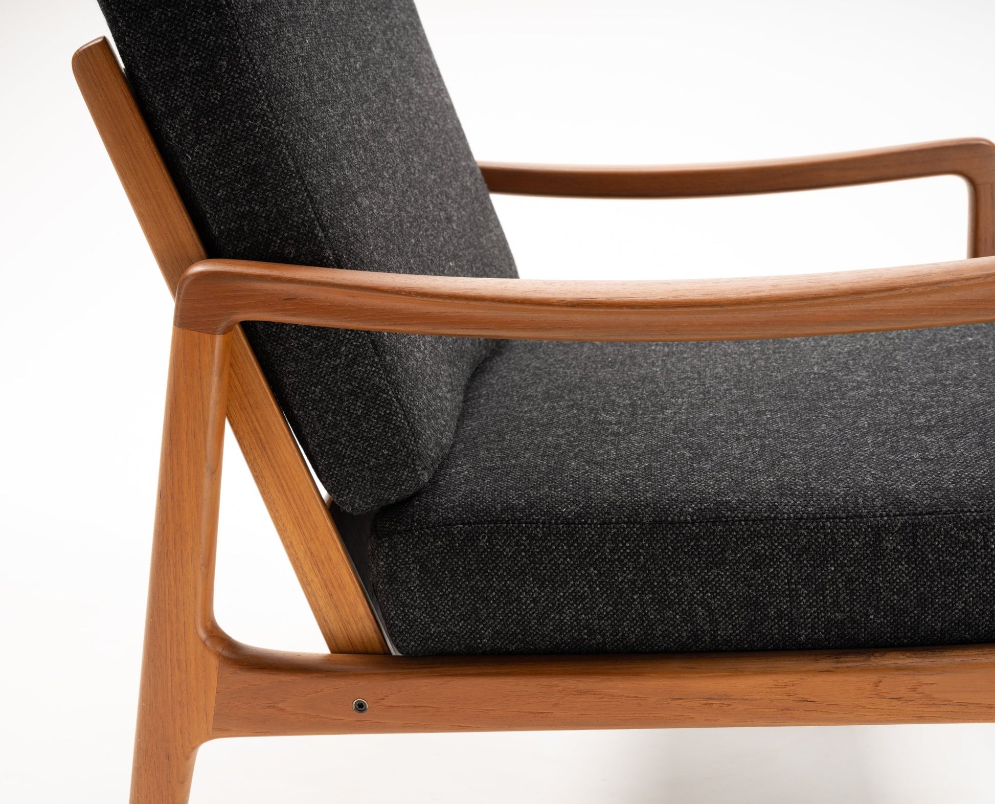 Close-up of Ole Wanscher rocking chair with solid teak frame and dark upholstered cushions, mid-century Danish design.