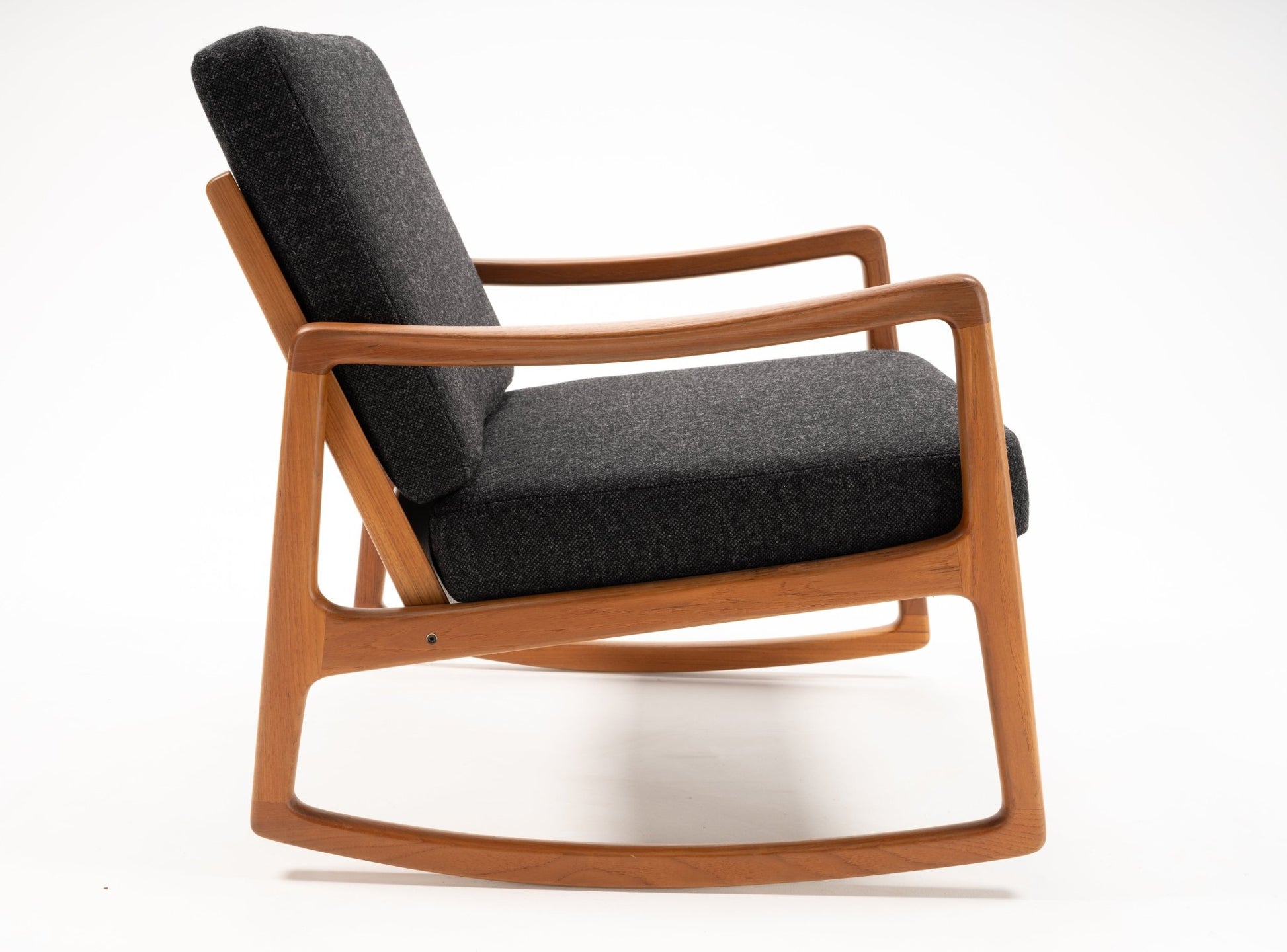 Ole Wanscher rocking chair in teak with sculpted armrests and dark upholstered cushions on white background