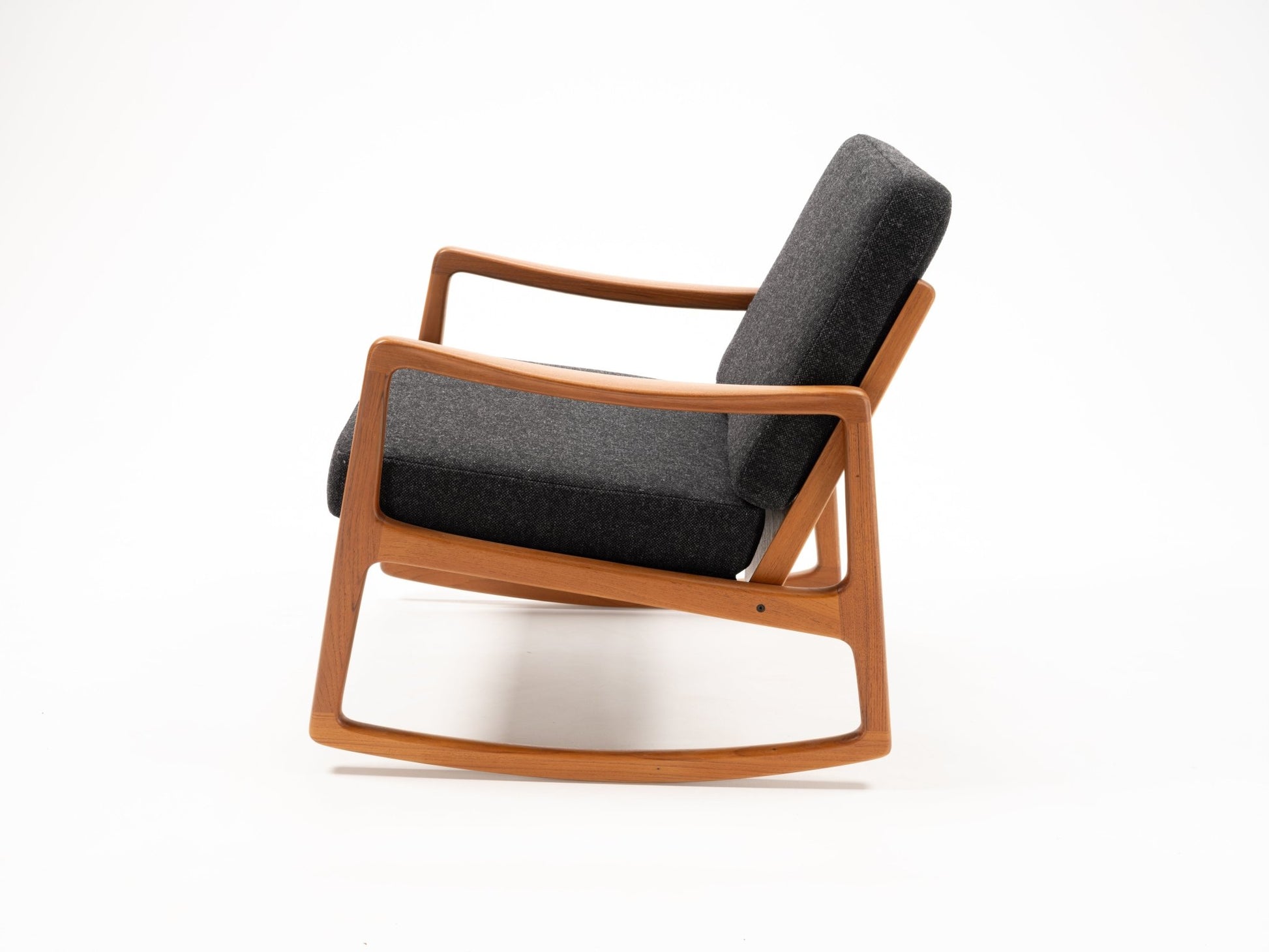 Ole Wanscher rocking chair with sculpted teak frame and dark grey upholstered cushions in minimalist style