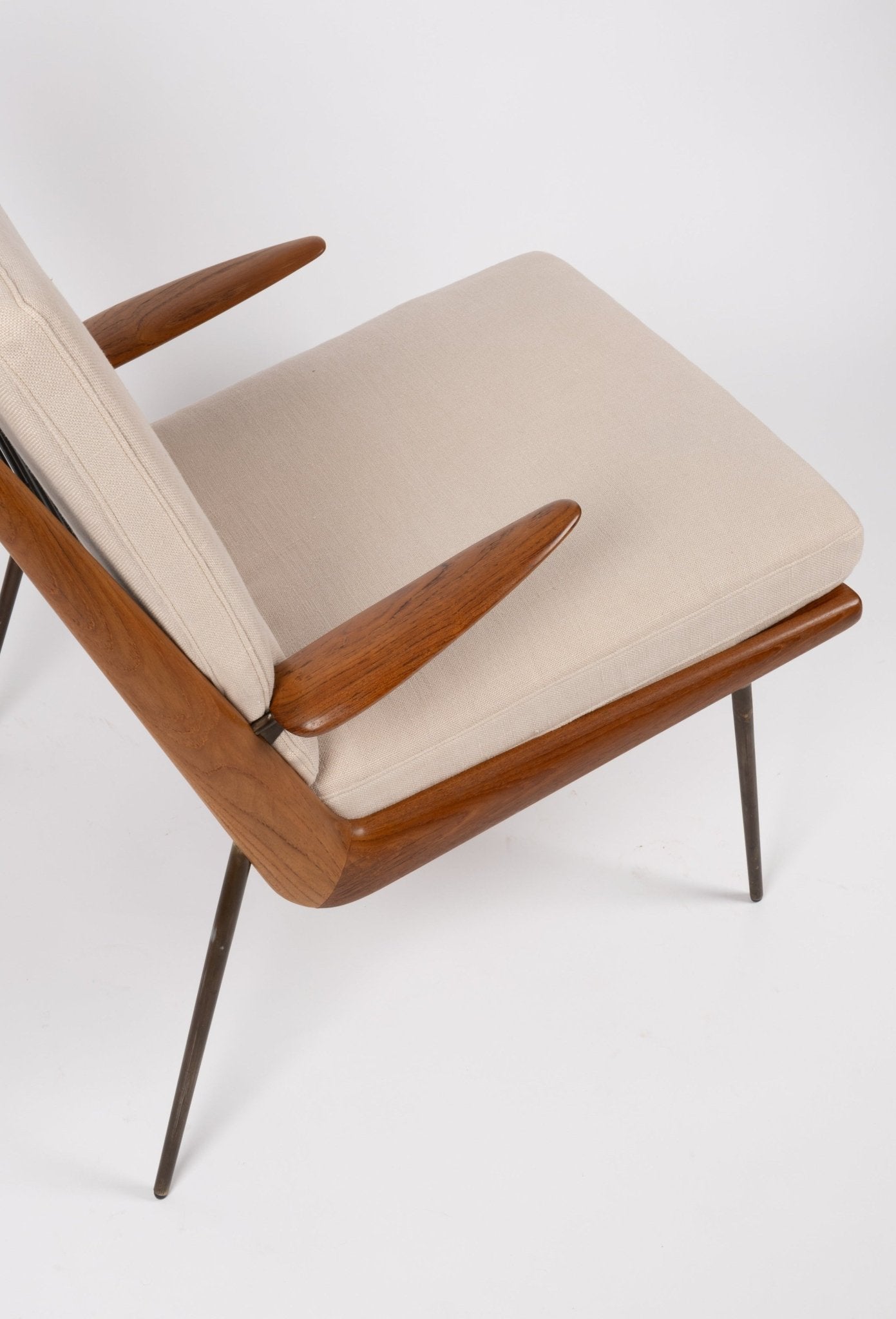 Mid-century modern teak and brass "Boomerang" armchair with beige upholstered seat and angled legs on white background.
