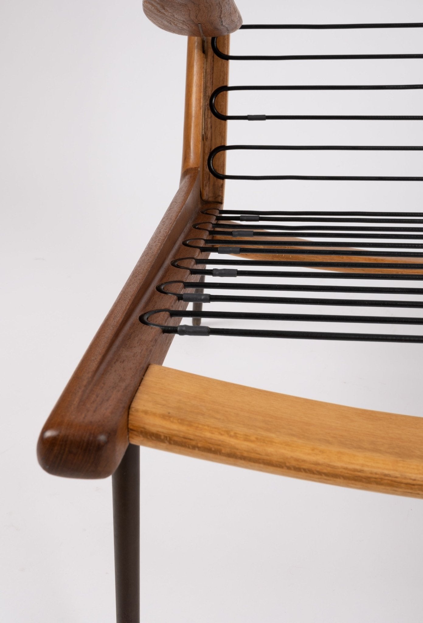 Close-up of Peter Hvidt Boomerang armchair showing curved teak frame and black metal spring suspension system