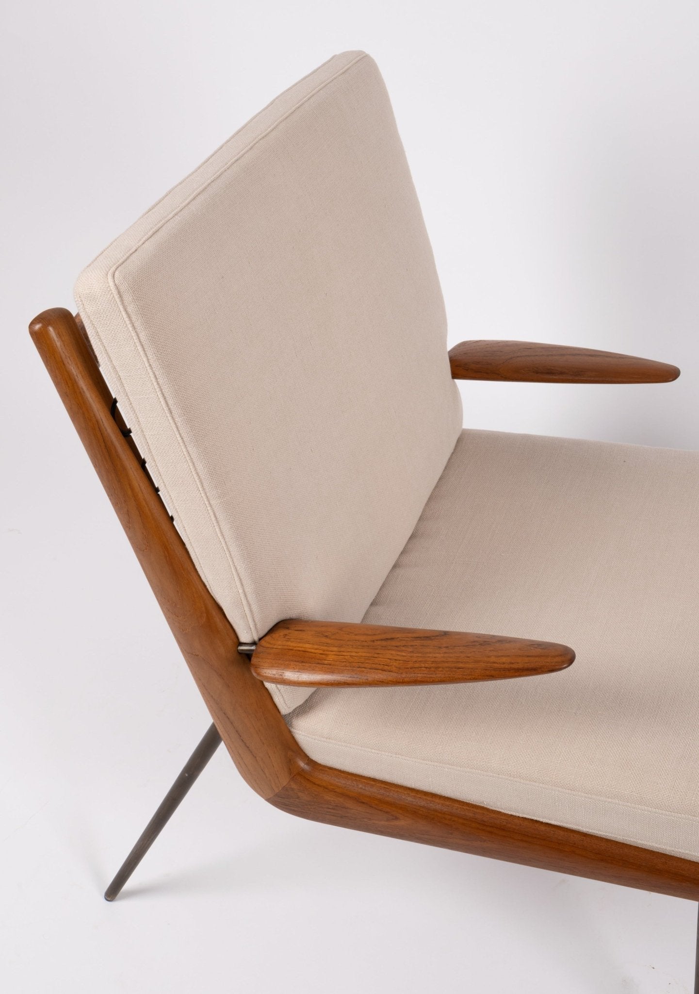 Close-up of Peter Hvidt "Boomerang" armchair with teak wood frame, curved armrests, beige cushions, and brass legs