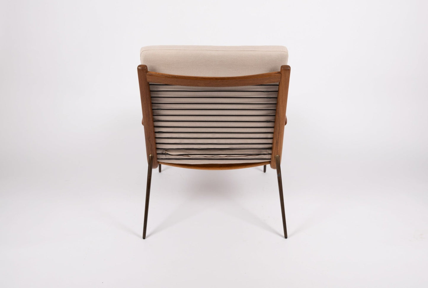 Peter Hvidt "Boomerang" armchair with teak frame, brass legs, and beige cushioned backrest shown from rear view.