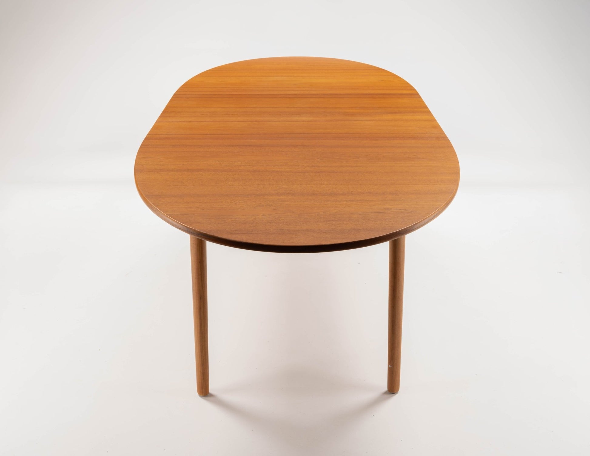 Peter Hvidt Model 311 mid-century modern extendable teak dining table with rounded top and tapered legs on white background