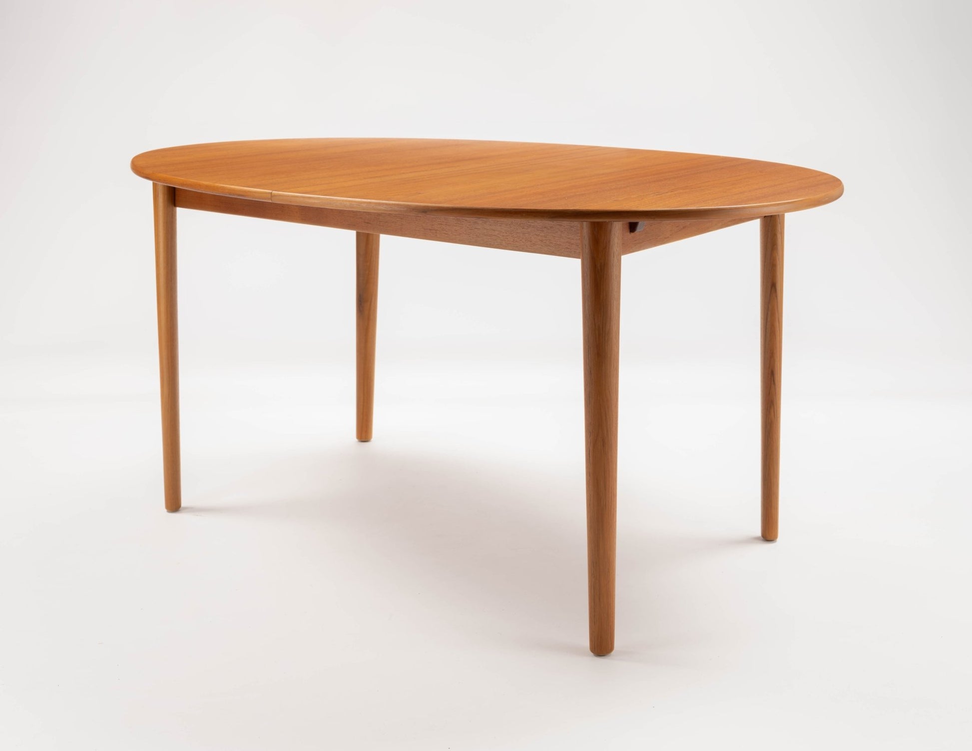 Peter Hvidt Model 311 extendable teak dining table with round top and tapered turned legs on white background