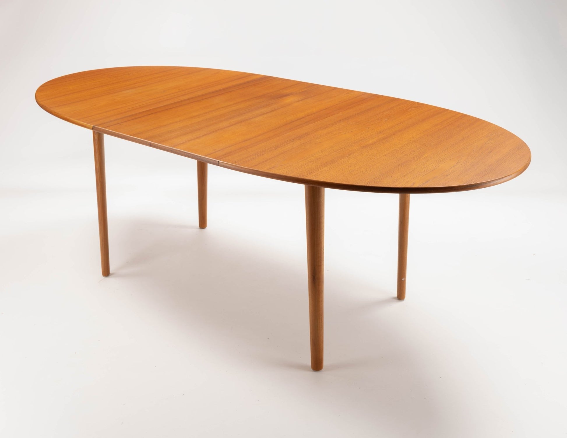 Peter Hvidt mid-century modern teak dining table with round top and tapered turned legs on white background