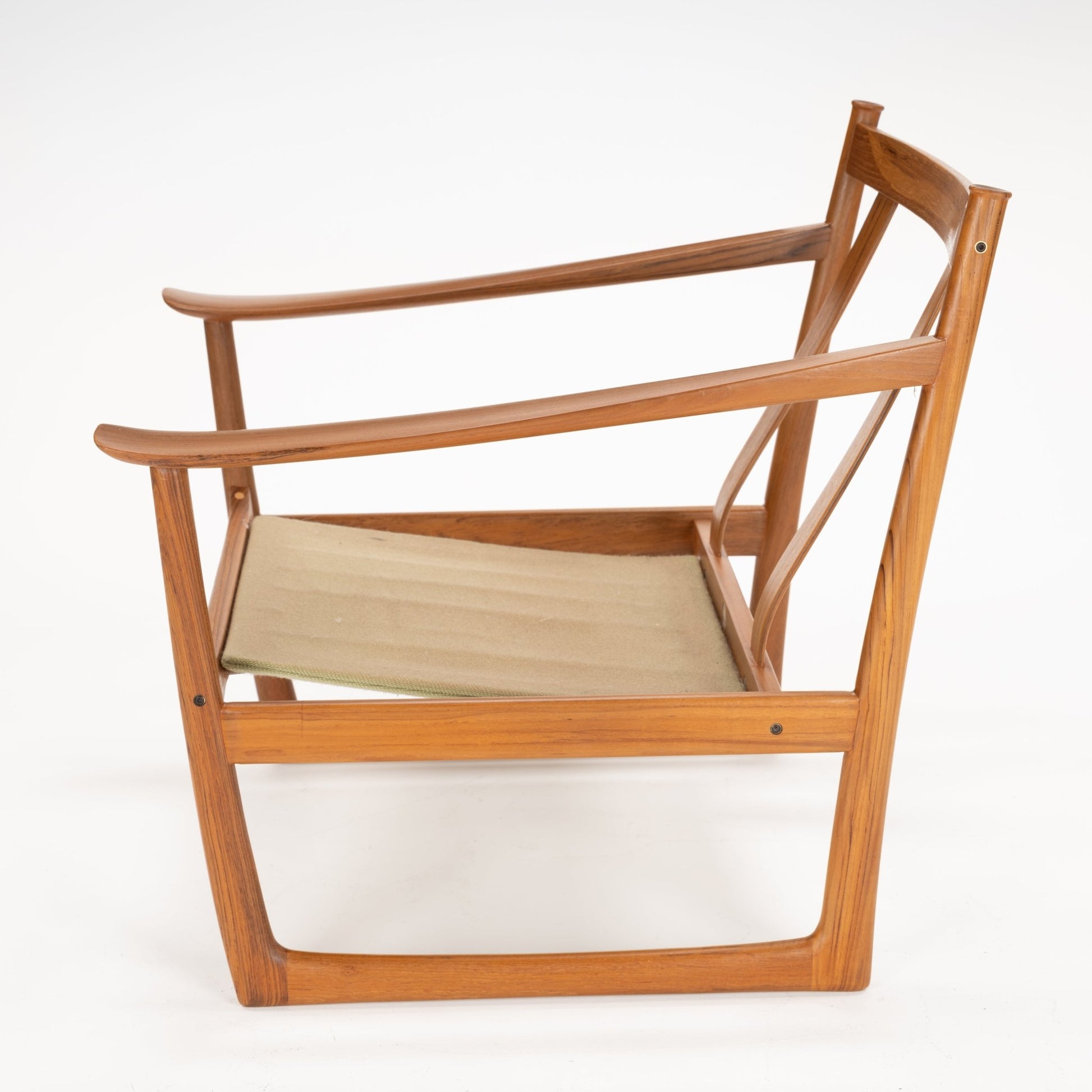 Side view of wooden chair frame with curved armrests and beige fabric sling seat on white background