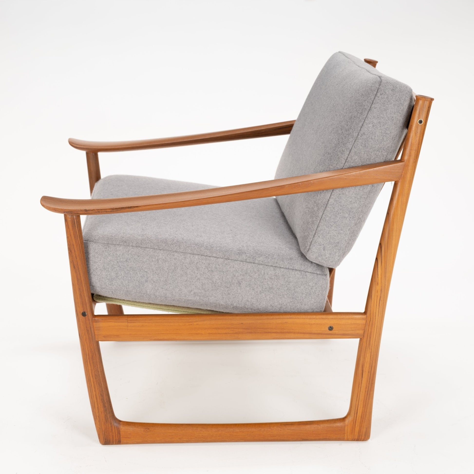 Side view of a wooden framed armchair with light grey cushioned seat and backrest on a white background